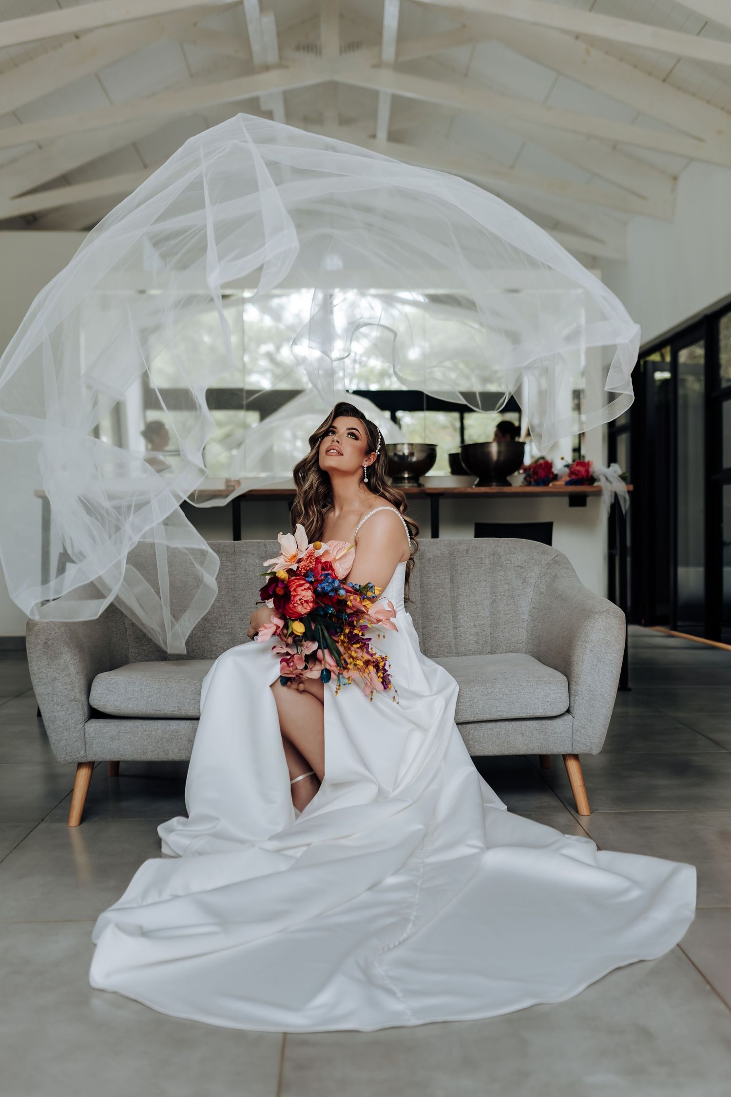 Bride in flowing white dress and veil twirling in modern white interior space.