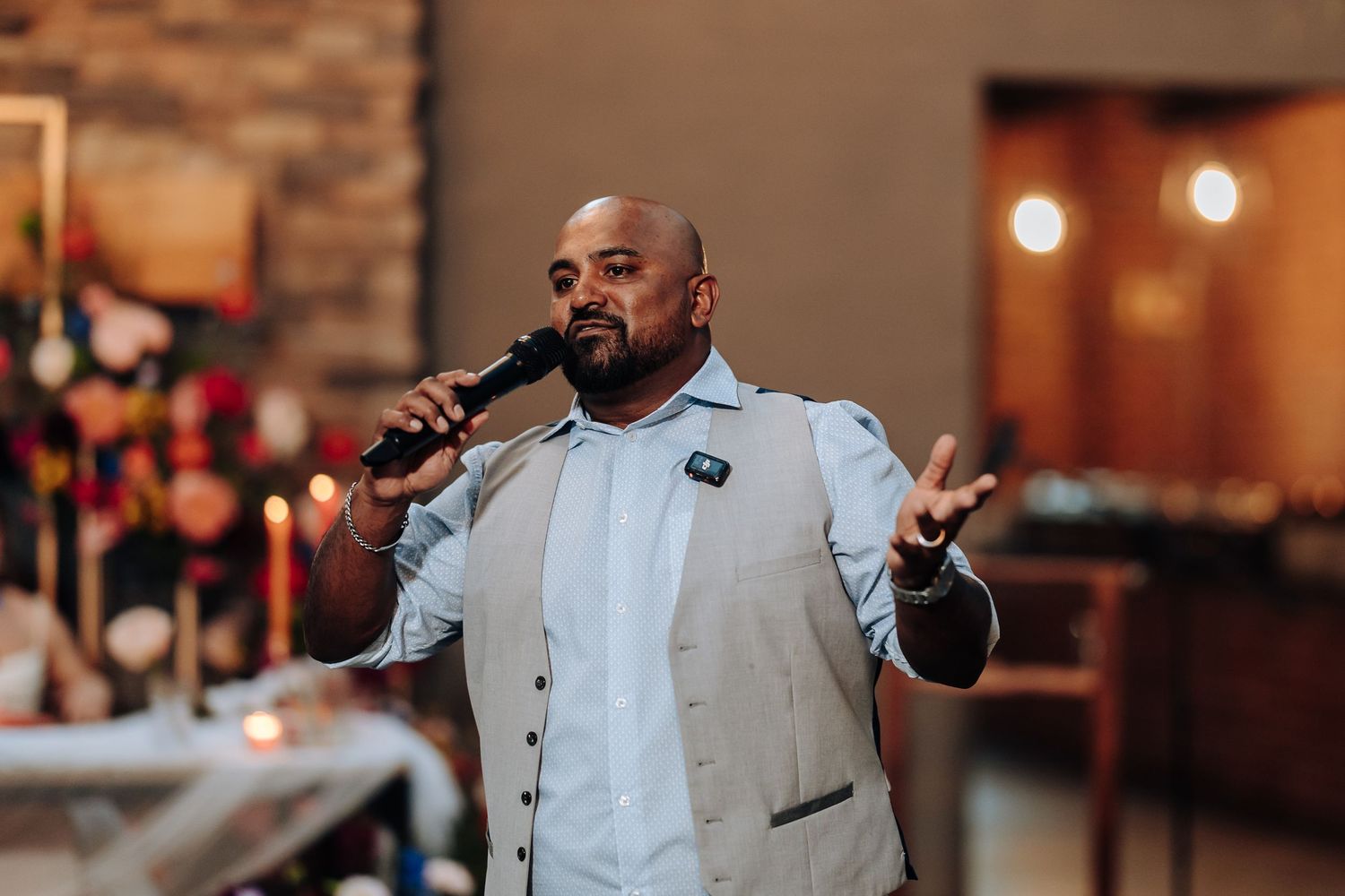 A performer in a light colored suit sings passionately into a microphone at a wedding reception.