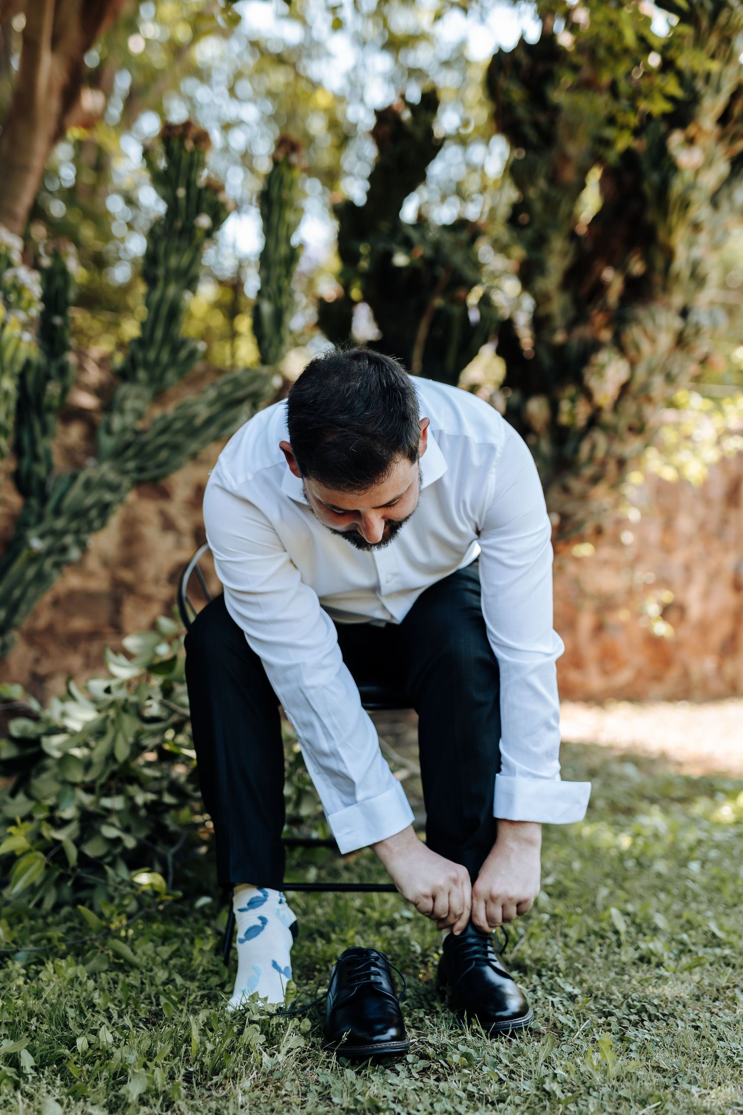 Person in white dress shirt and dark pants crouches on grass in outdoor setting.
