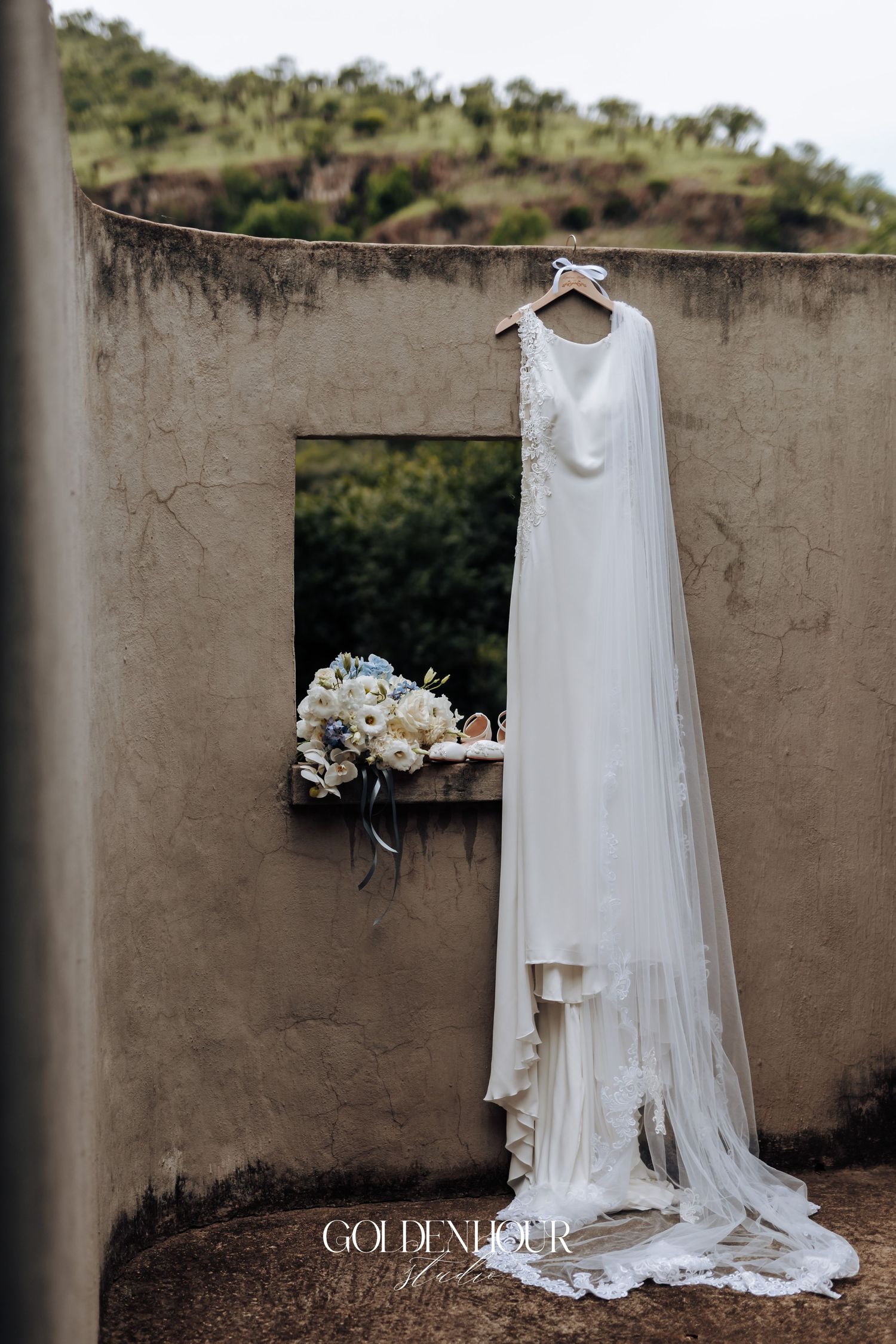 White wedding dress hanging against a stone wall with floral bouquet details.