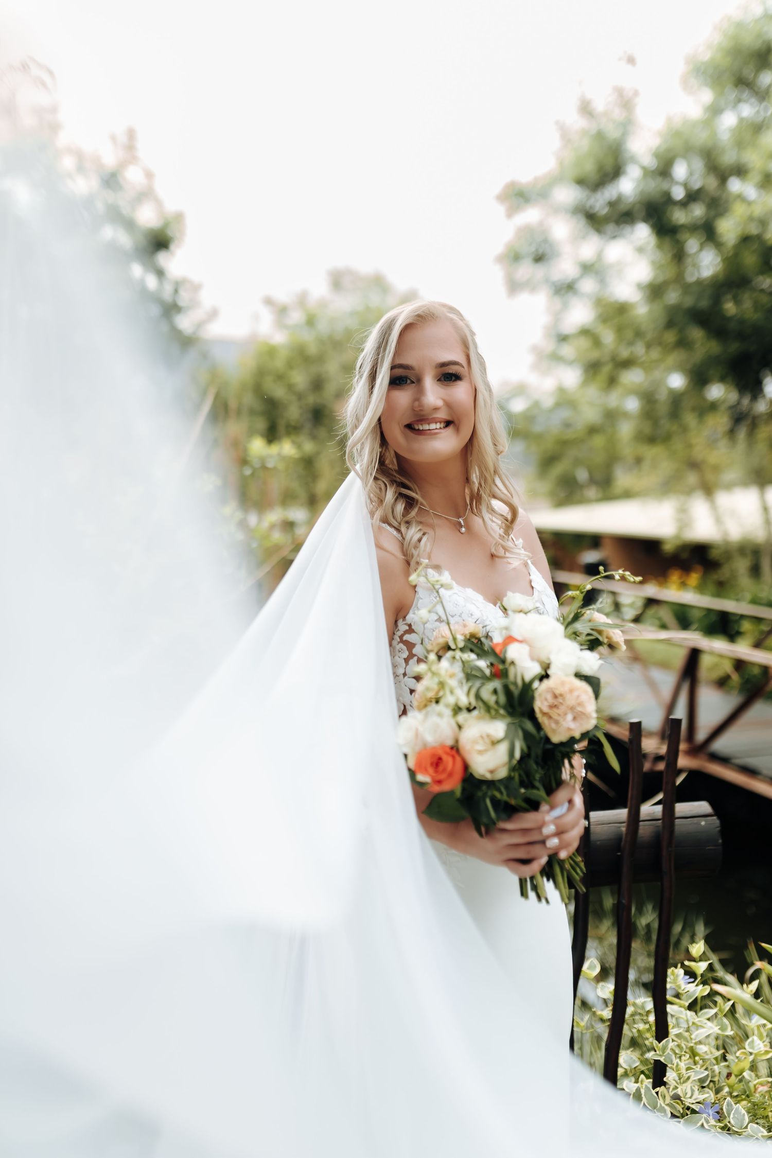 Beautiful bride in white wedding dress holds colorful bouquet while standing outdoors on a sunny day.