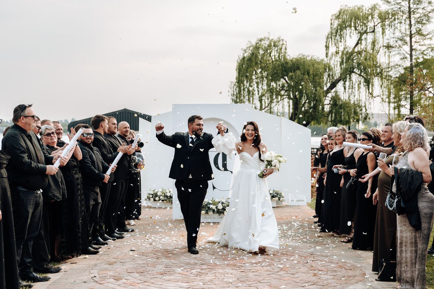 A wedding party celebrates on a beach with guests throwing flower petals during a joyful exit ceremony.