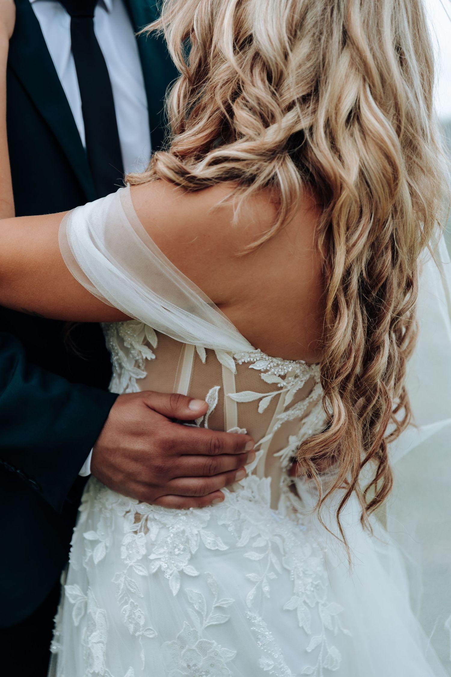 Close-up views of a white wedding dress with delicate lace details and a bow tied at the back.