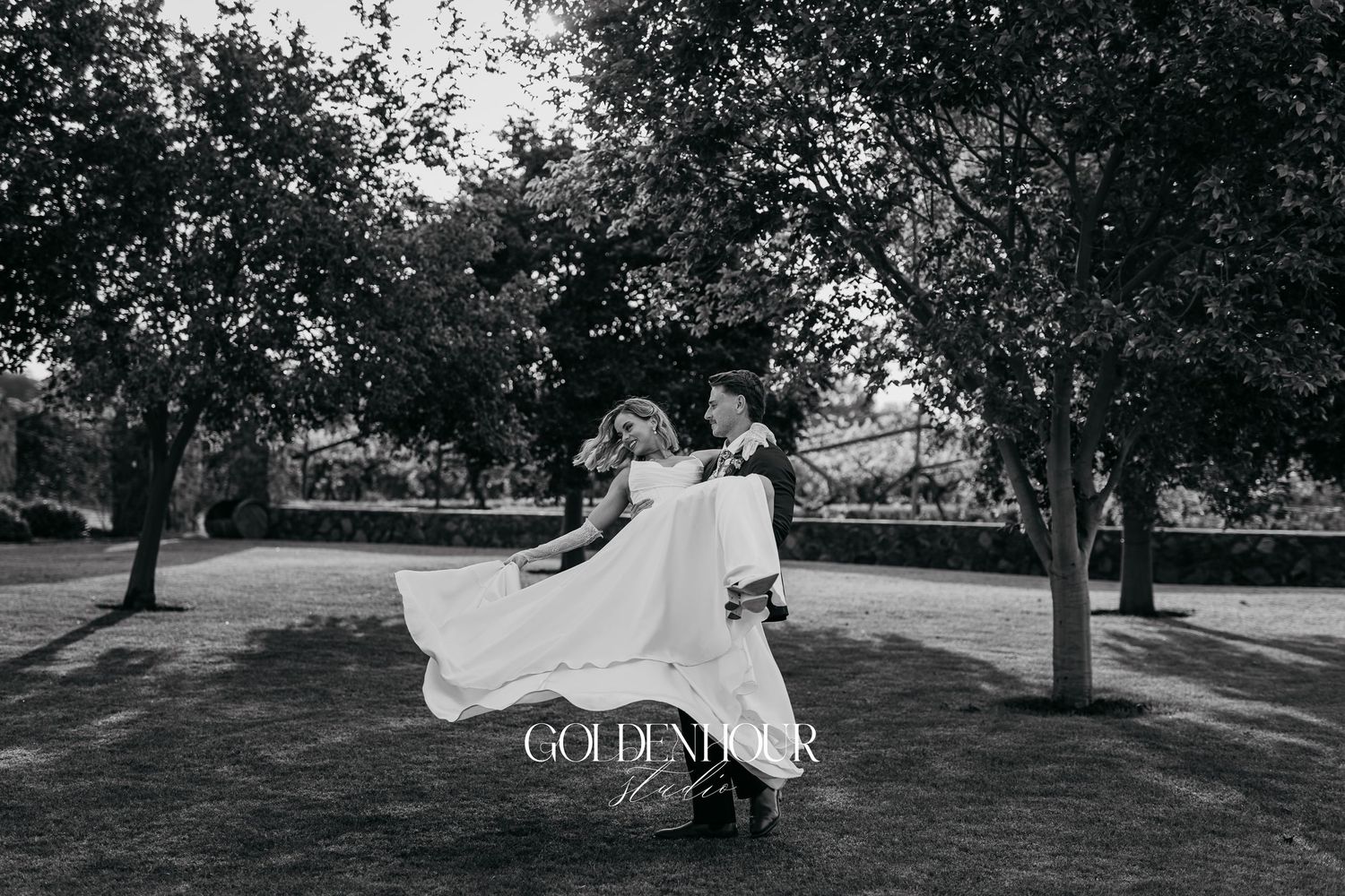 Artistic black and white photo of wedding party dancing in an outdoor garden setting.