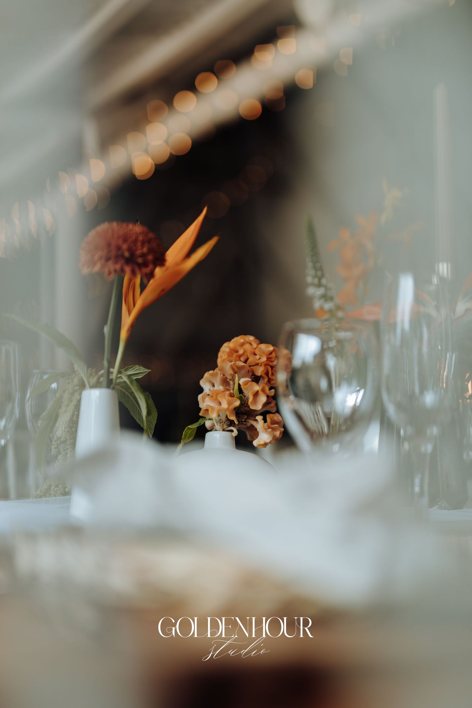 Elegant wedding reception table setting with wine glasses and floral arrangements in soft focus with bokeh lights.