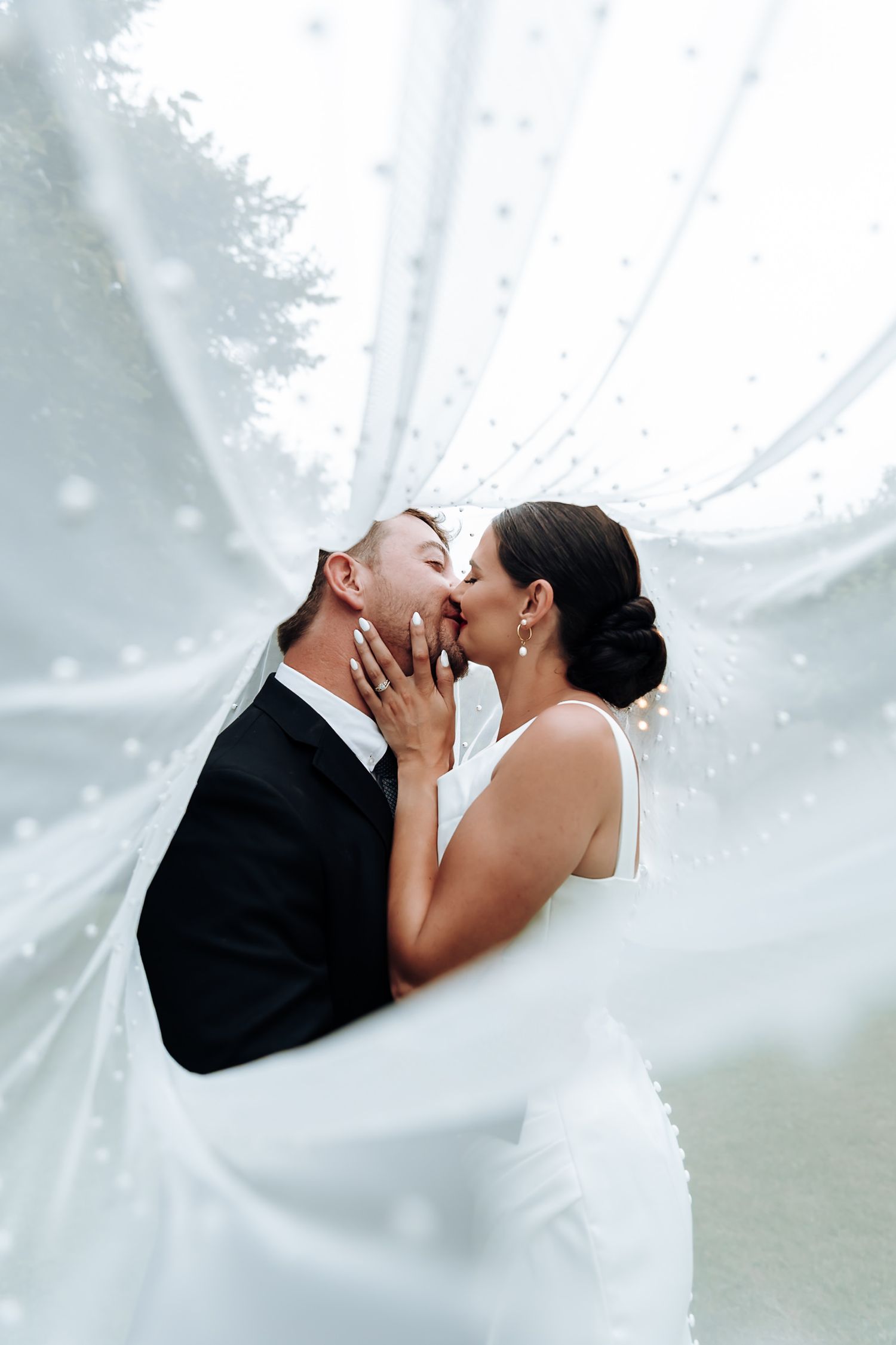 A romantic wedding couple shares a tender kiss behind flowing white veil fabric in three artistic detail shots.