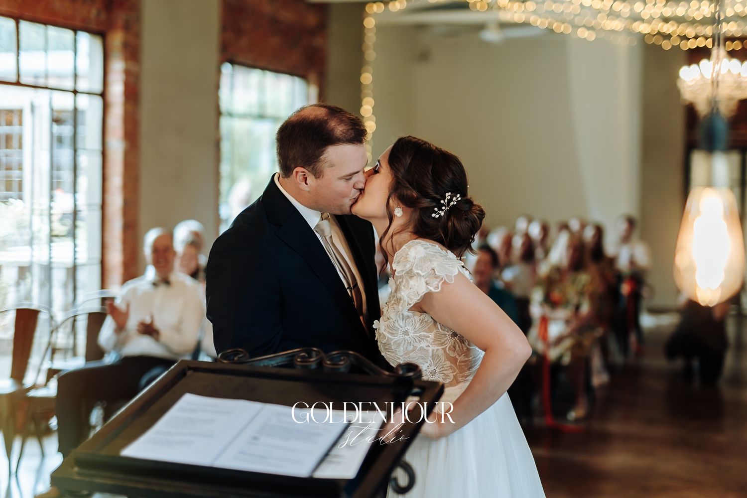Bride and groom share first kiss at elegant indoor wedding ceremony.