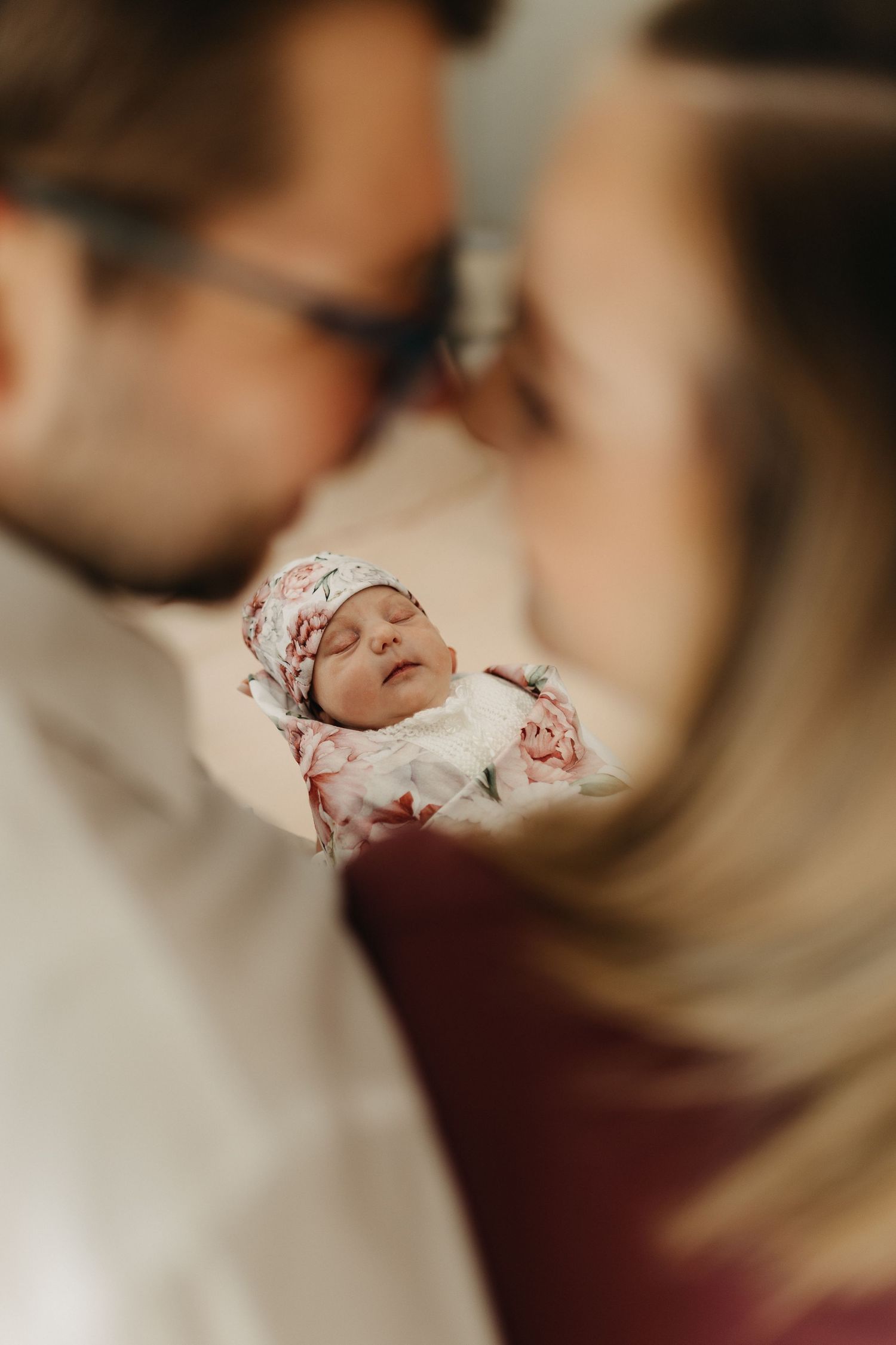 Close-up shot of baby swaddled in floral print blanket against blurred background.