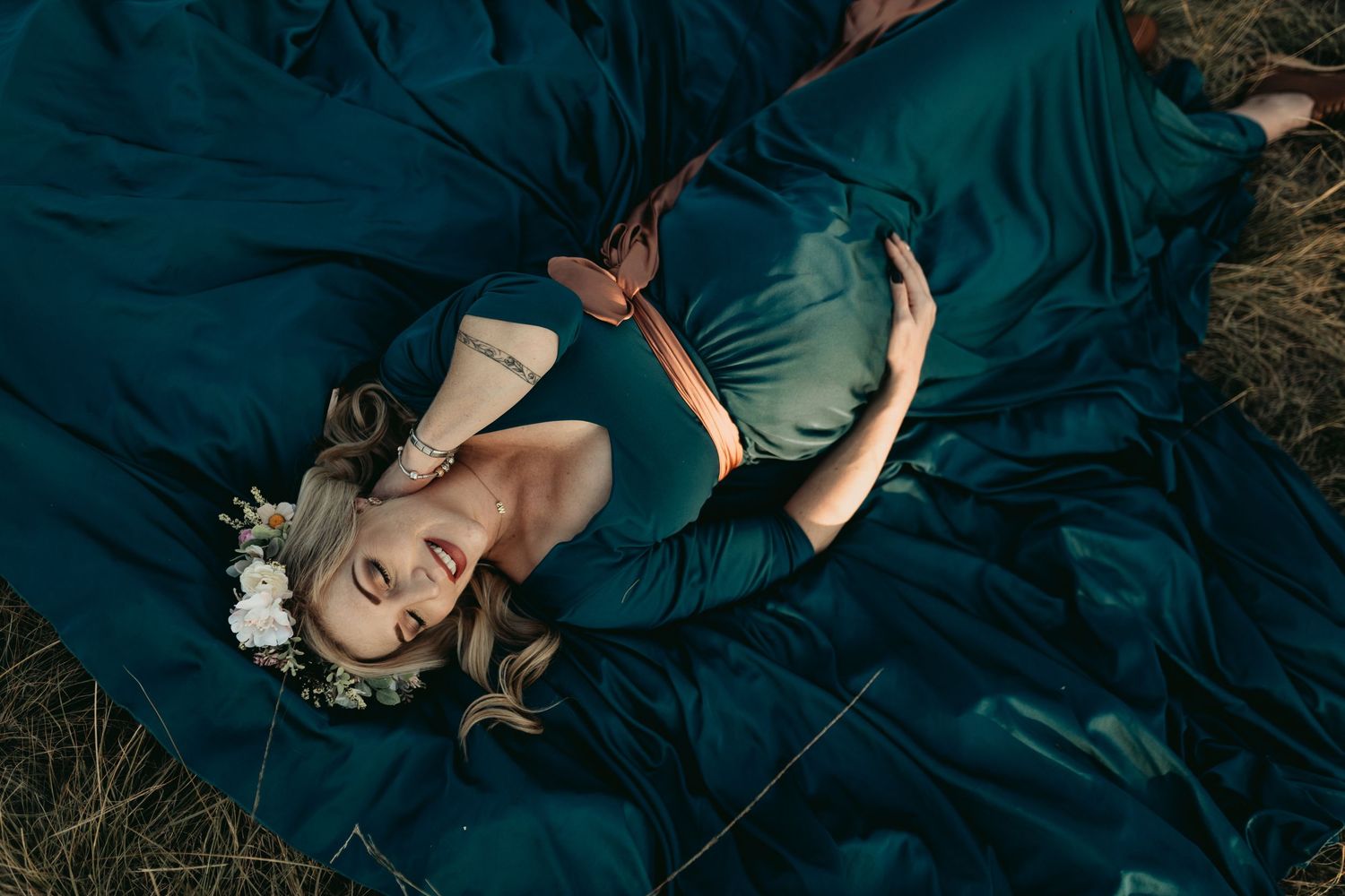 A person in a dark teal dress laying in grass during a dreamy outdoor photo session.