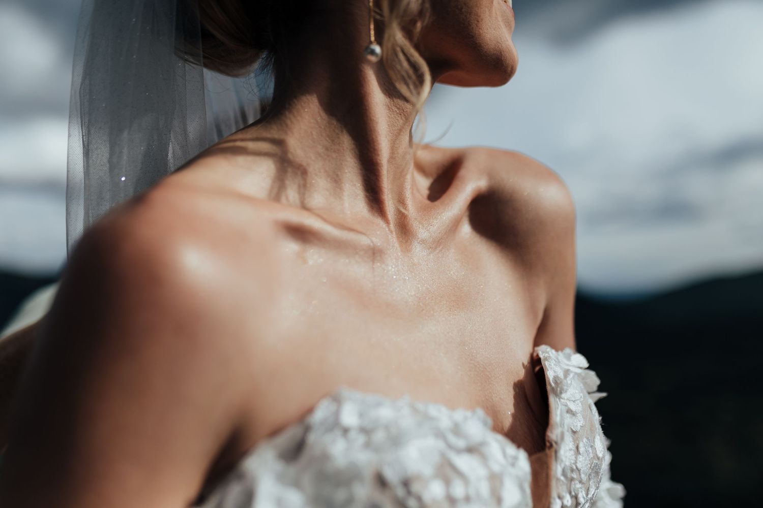 Bride in a white strapless gown with delicate lace details and floral appliques in front of gray backdrop.