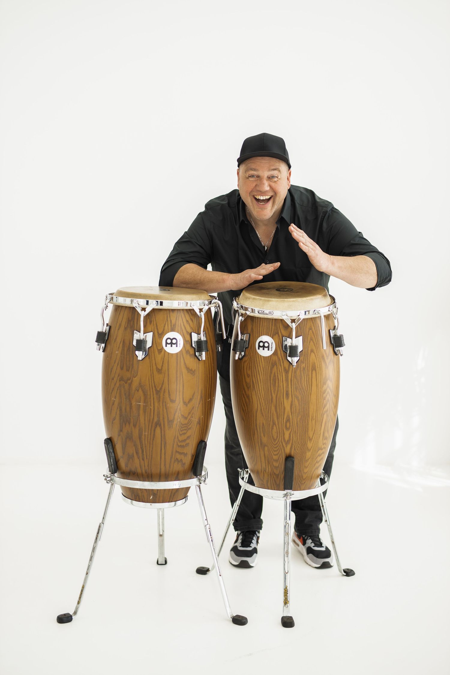 A musician poses playfully with wooden conga drums on a white background in a series of shots.