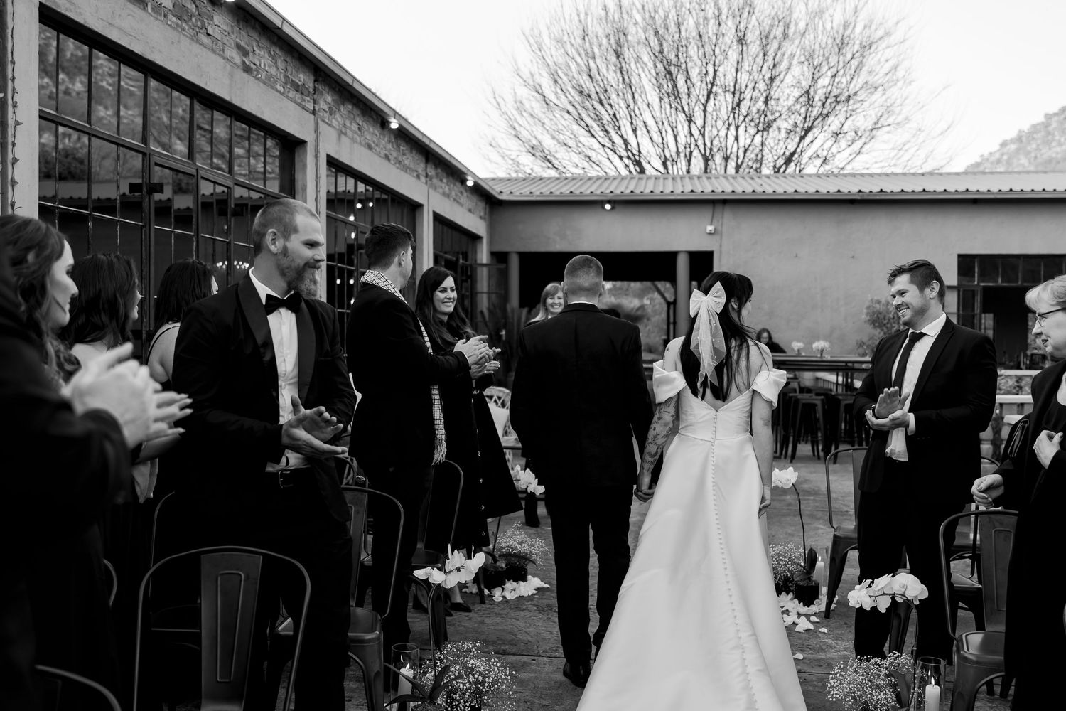 Black and white wedding photograph at a rustic venue with guests mingling in an outdoor courtyard setting.