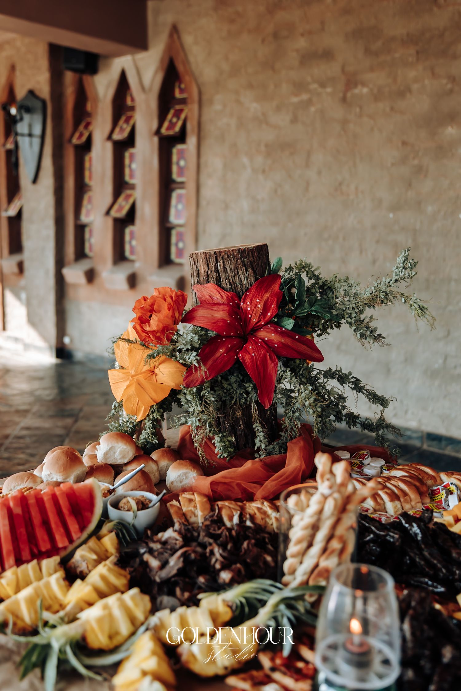 Elegant wedding grazing table with tropical floral centerpiece on wood stump, surrounded by fruit and appetizers.
