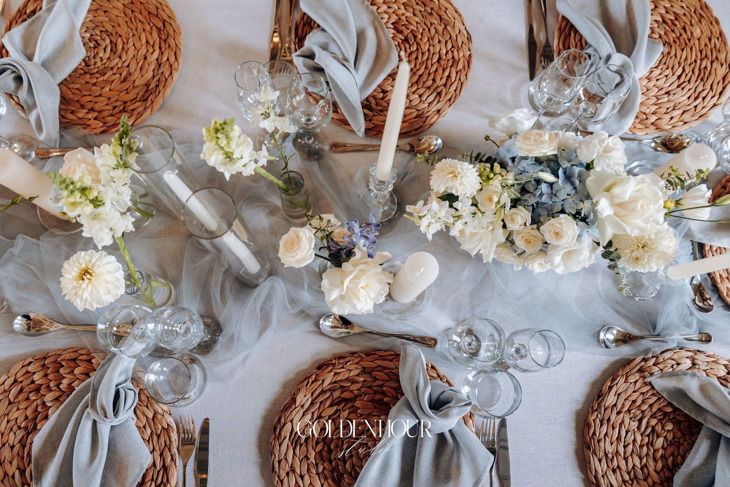 Elegant wedding centerpiece with white hydrangeas, roses and natural woven spheres arranged on a mirrored surface.