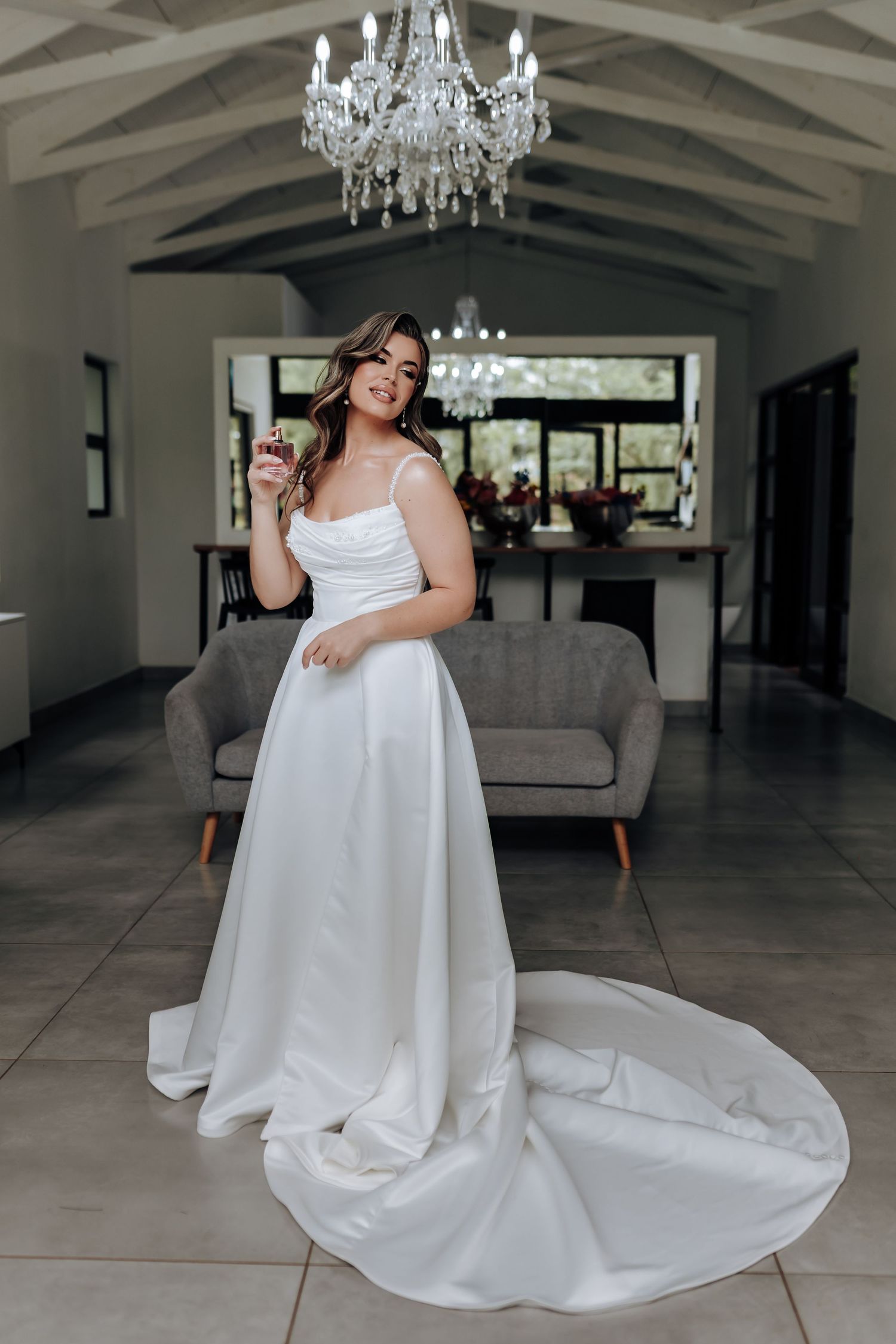 Elegant white wedding dress with flowing train photographed in a modern room with crystal chandelier and wood beams.