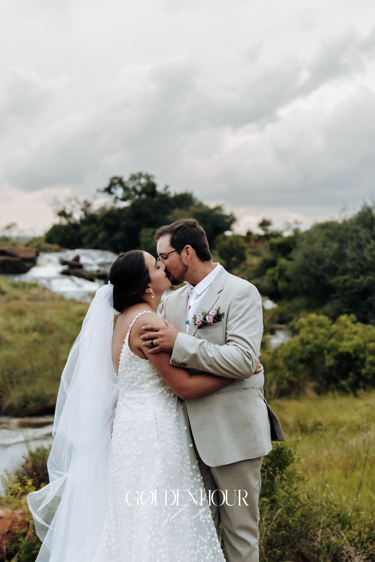 Romantic wedding couple embracing on a hilltop with cloudy sky backdrop.