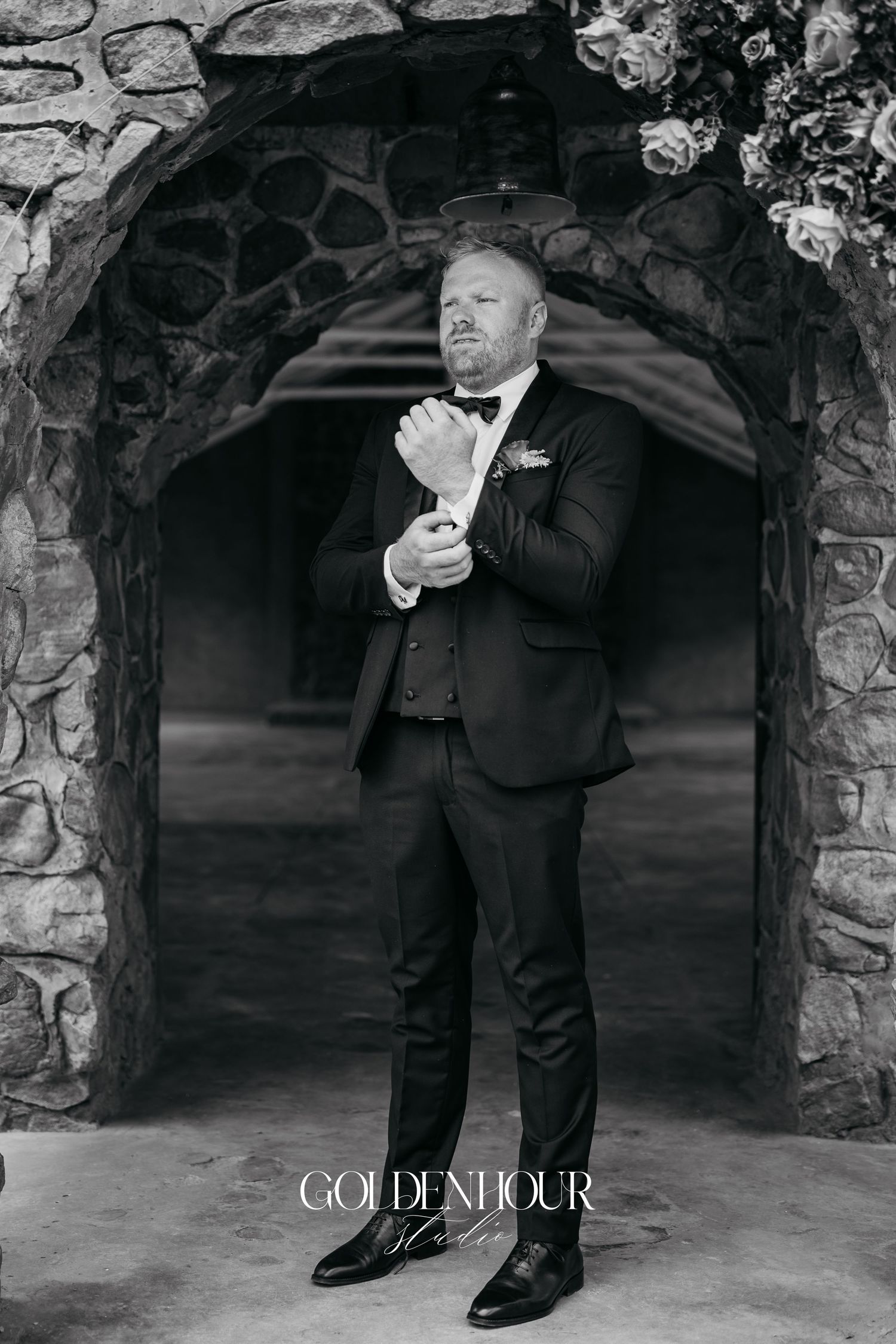 A man in a formal black suit strikes three different poses against a stone archway backdrop.