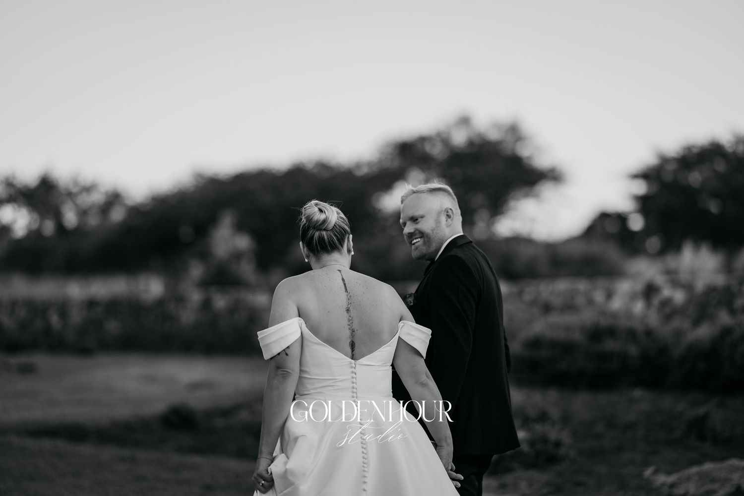 A black and white outdoor wedding photo of a couple walking together in a garden setting.