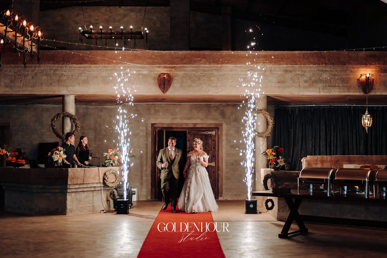 Bride and groom make grand entrance on red carpet with sparkling fountain fireworks indoors.