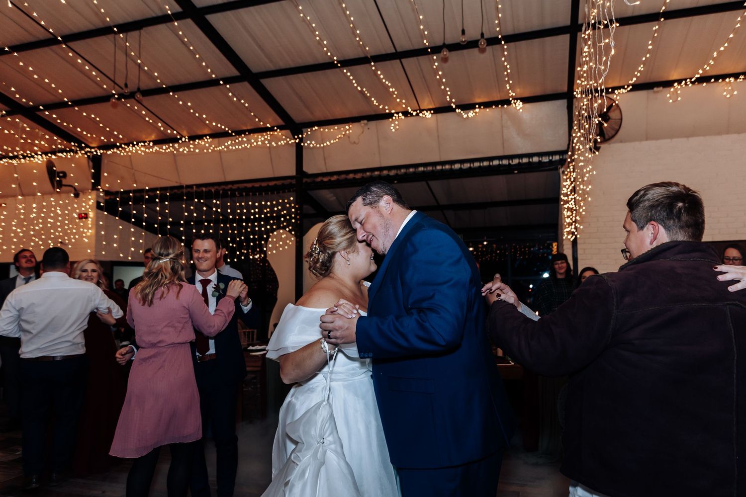 Bride and groom share first dance under twinkling fairy lights at romantic indoor wedding reception.