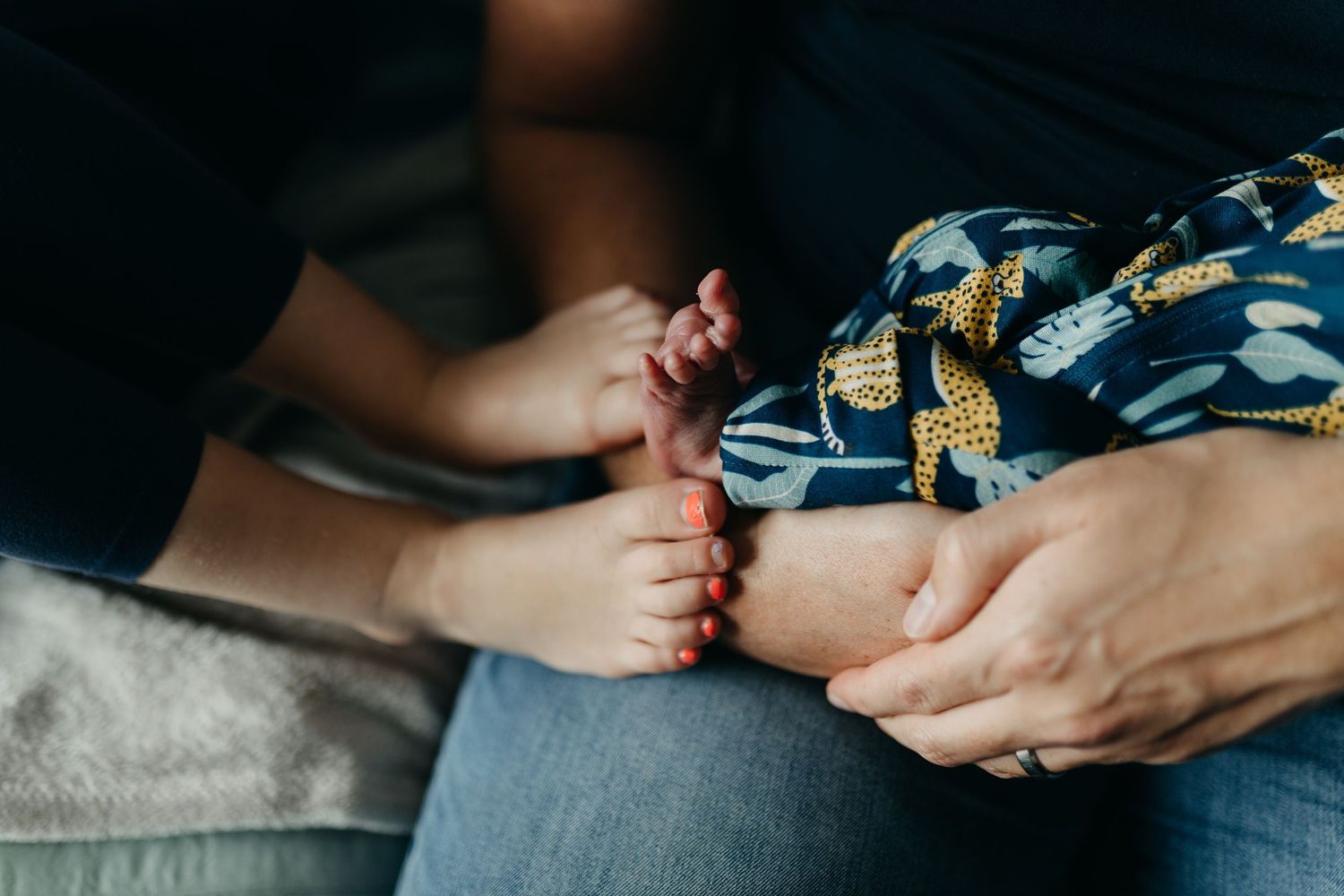 Close up shots of tiny newborn feet and loving hands against blue bedding in natural light.