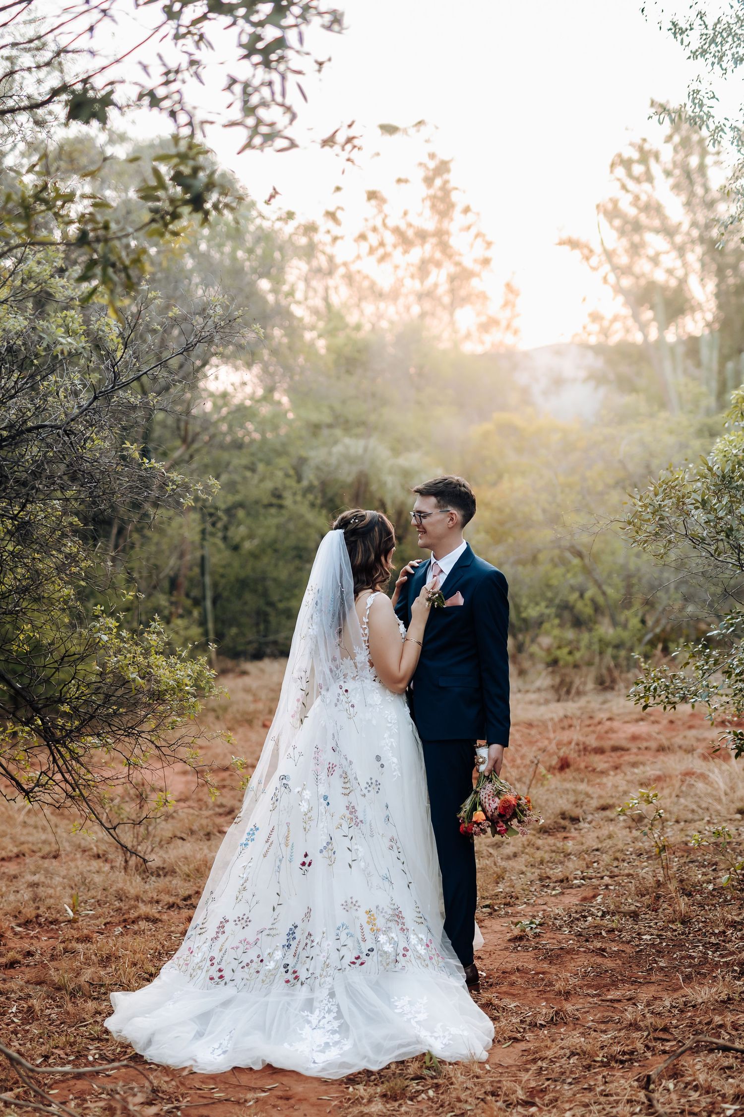 A romantic outdoor wedding photo series shows a couple in formal attire embracing on rustic terrain at sunset.