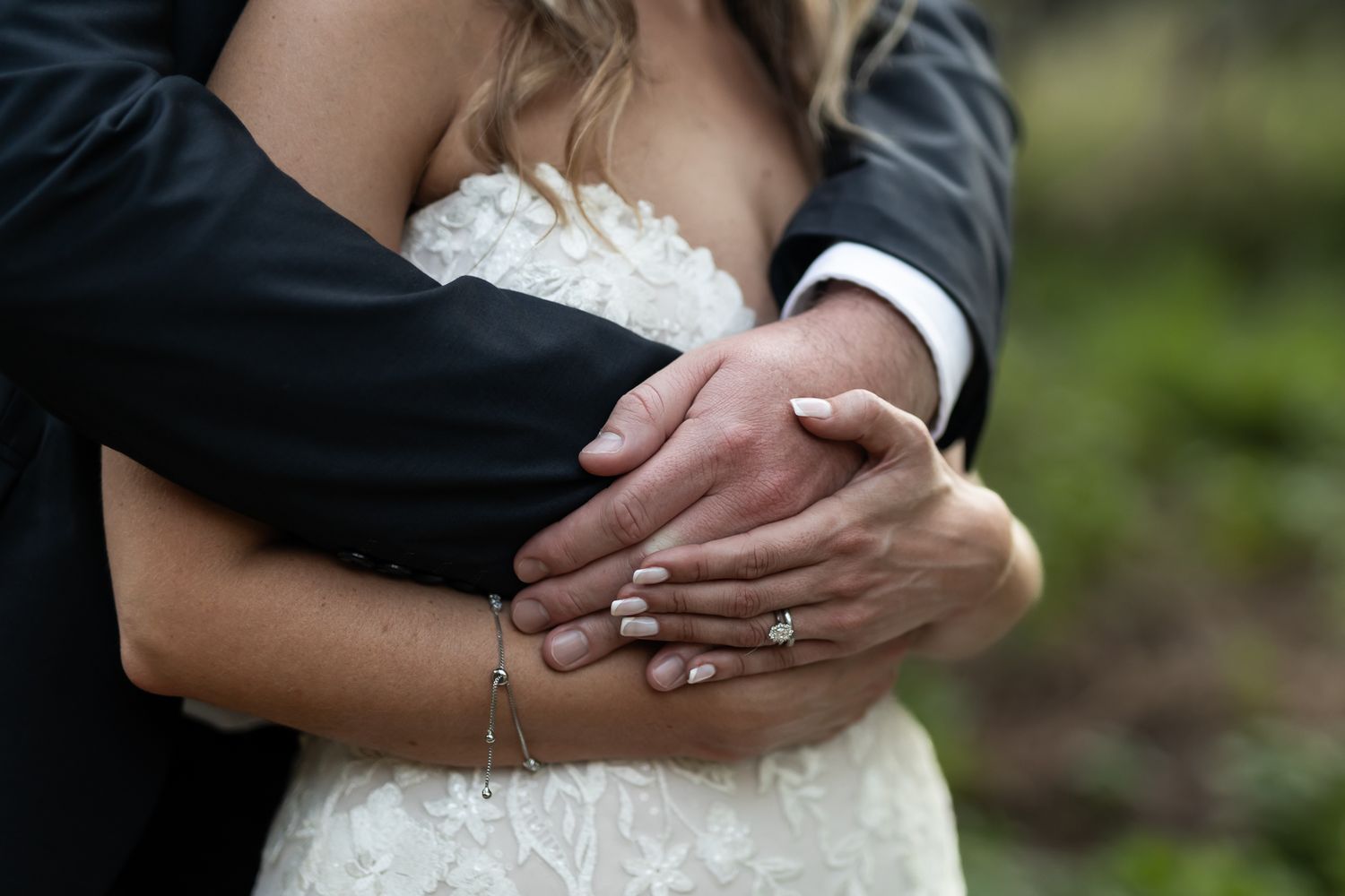 Close-up of wedding rings and embracing hands against formal wedding attire.
