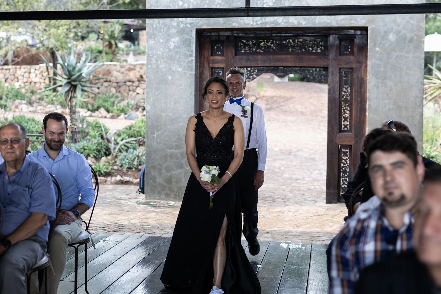 Wedding party member in black dress walks down outdoor aisle during ceremony.