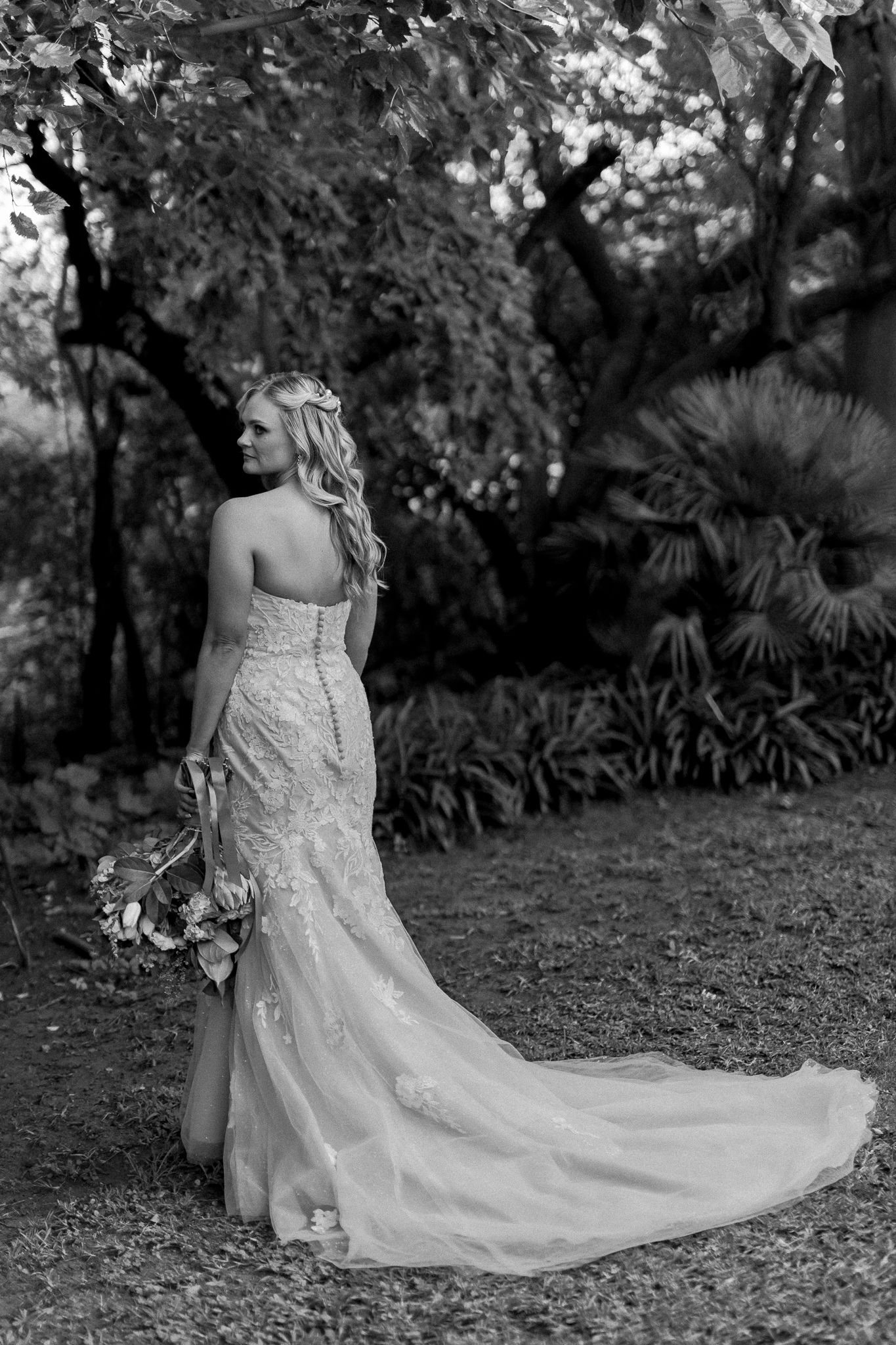A black and white bridal portrait showing the back of a lace wedding gown with a long train.