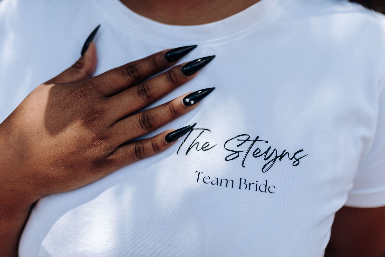 Manicured hand with black nails touching white t-shirt with Team Bride text.