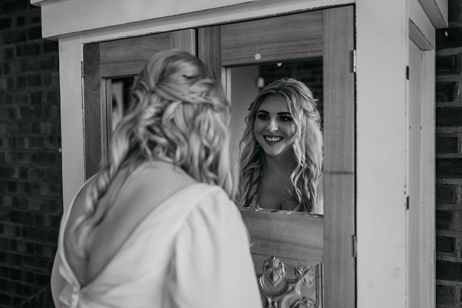 Black and white photo of bride looking at reflection in vintage mirror.