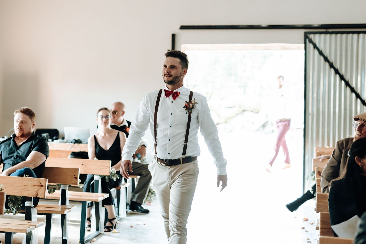 Groom walking confidently through venue space wearing suspenders and bow tie.