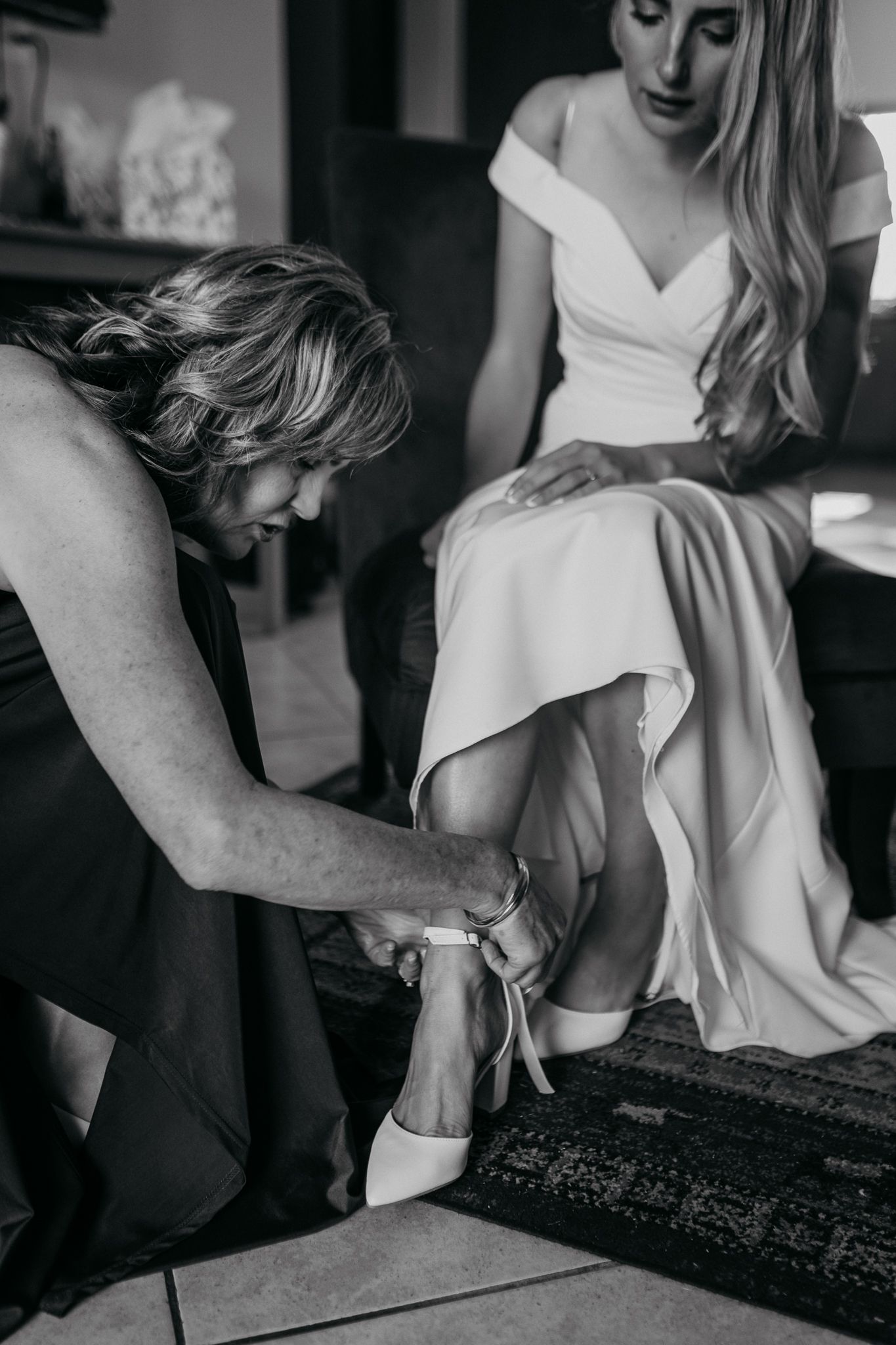 Black and white photo of final shoe adjustments during bridal preparation.