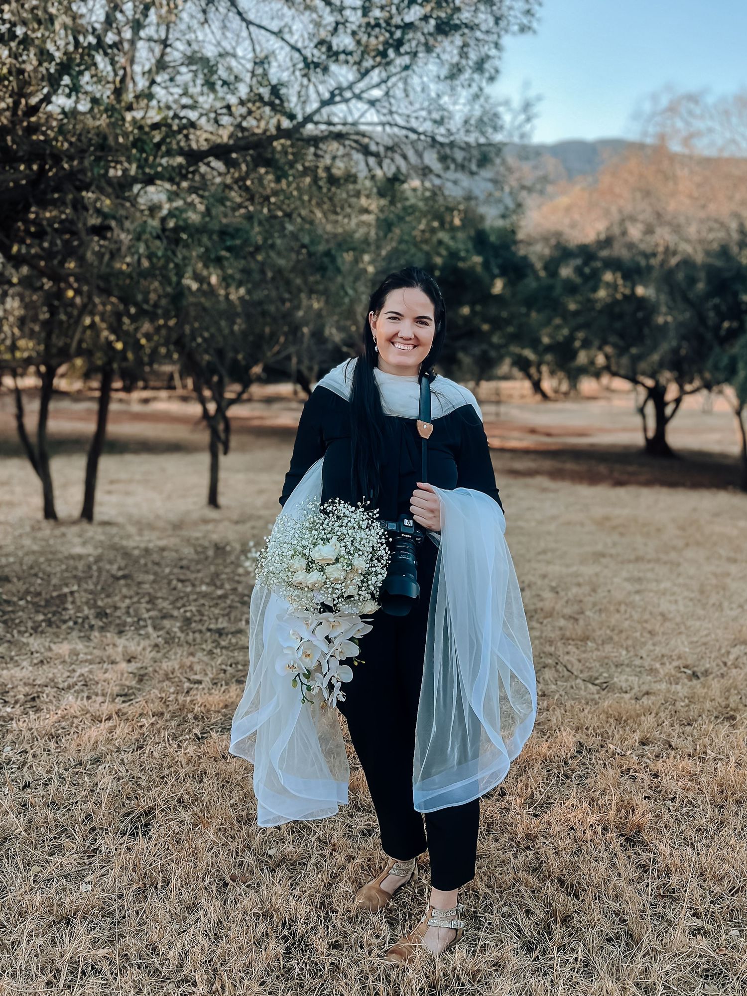 A photographer in navy attire holds a cascading white bouquet in an autumn orchard.