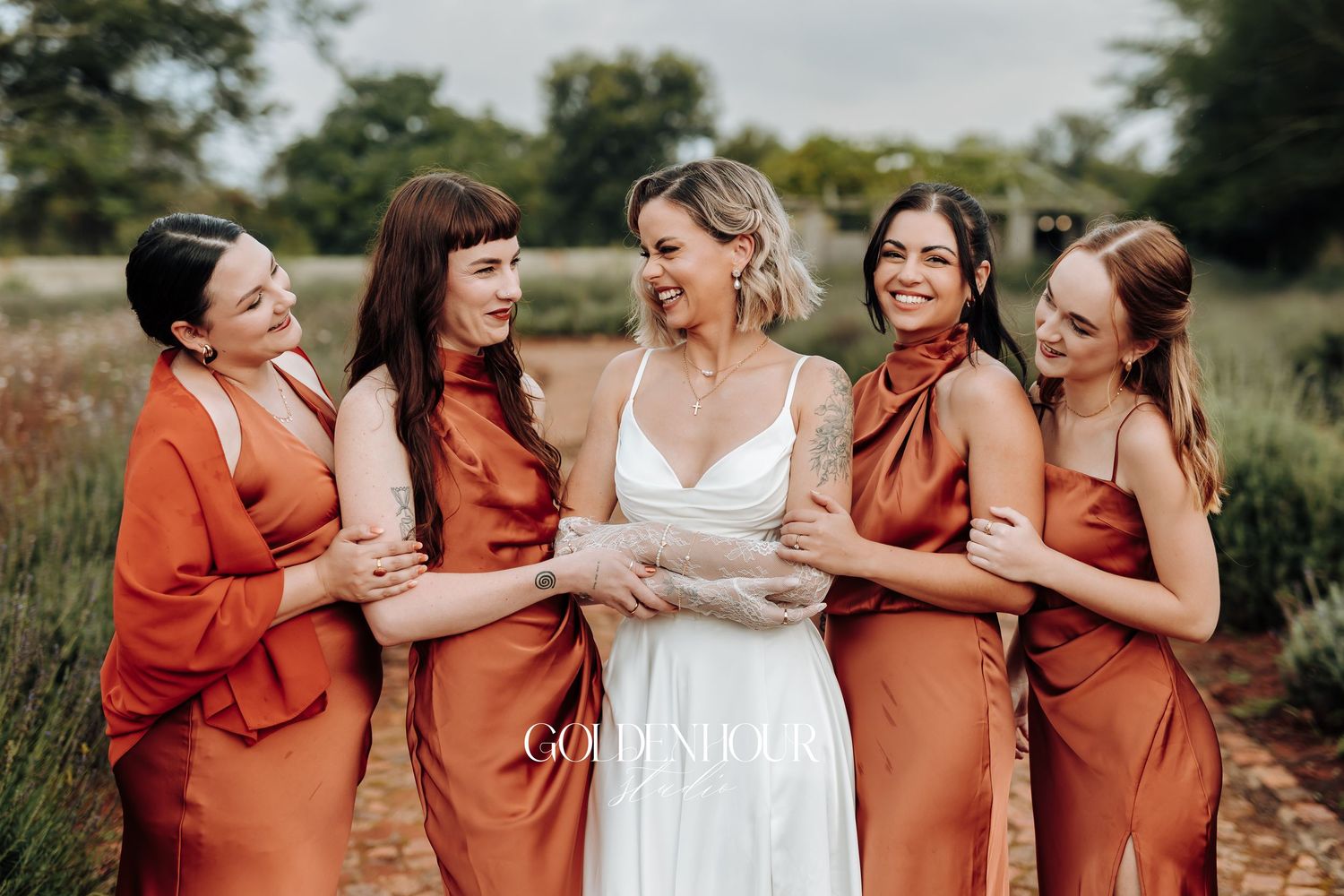 Wedding party in rust-colored dresses sharing joyful moment outdoors.