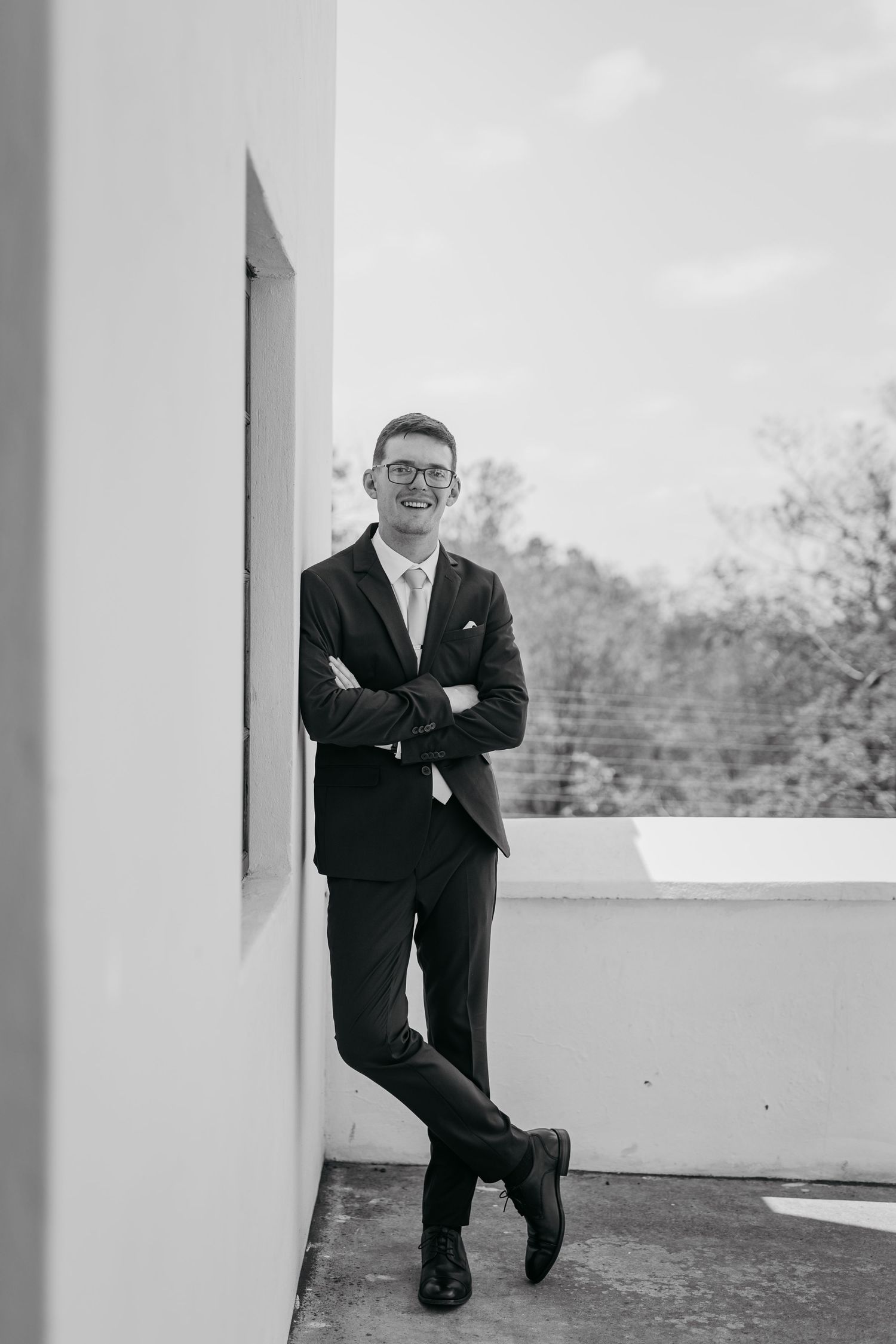 A person in a dark suit leans casually against a white architectural column in an outdoor setting.