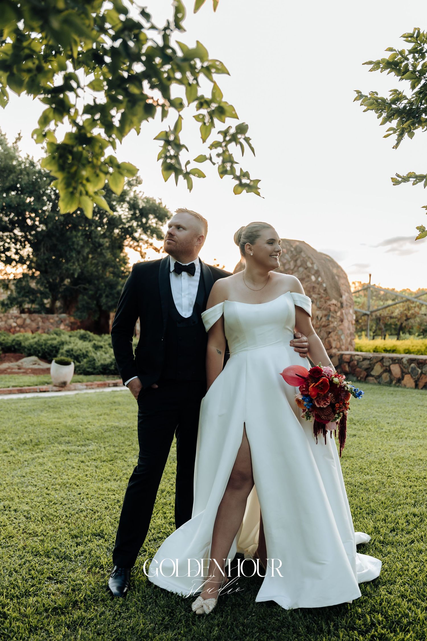 Romantic wedding couple embraces on a sunlit grassy lawn during golden hour photography session.