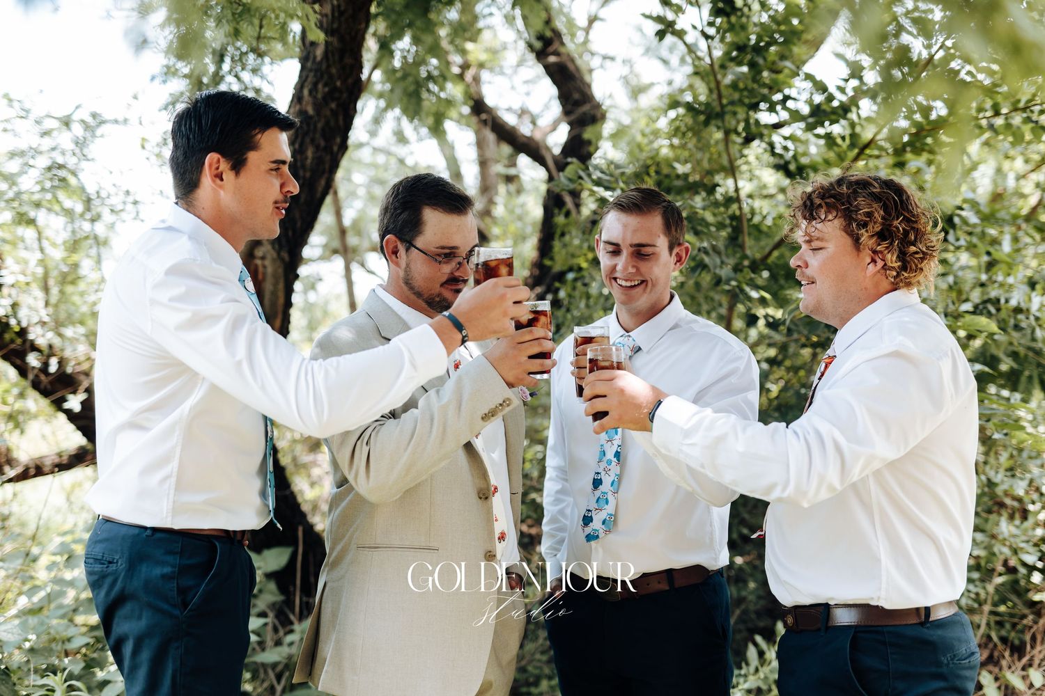 A group of groomsmen in white shirts share joyful moments while getting ready for a wedding outdoors.