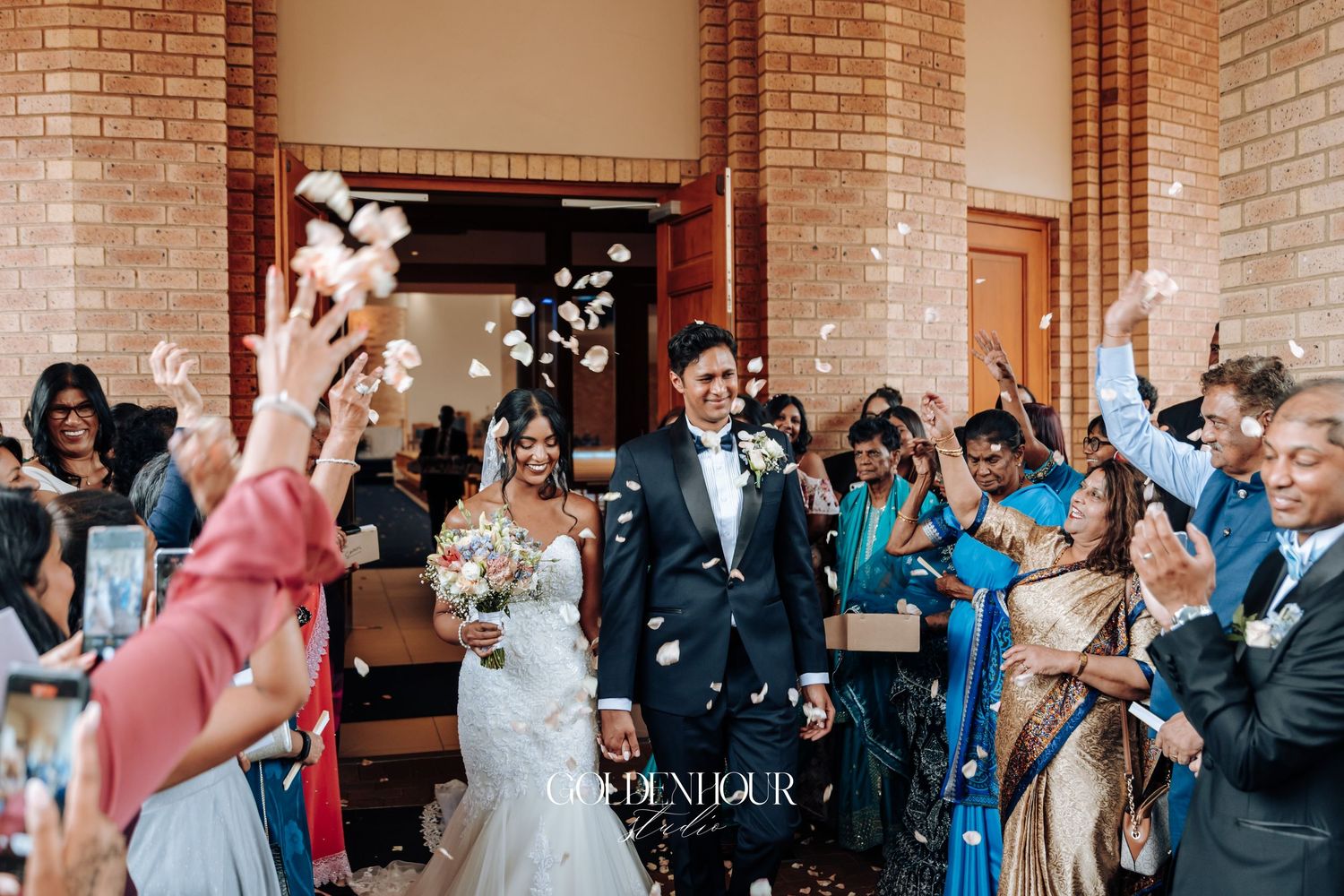 Joyful wedding celebration with guests throwing confetti outside brick building.