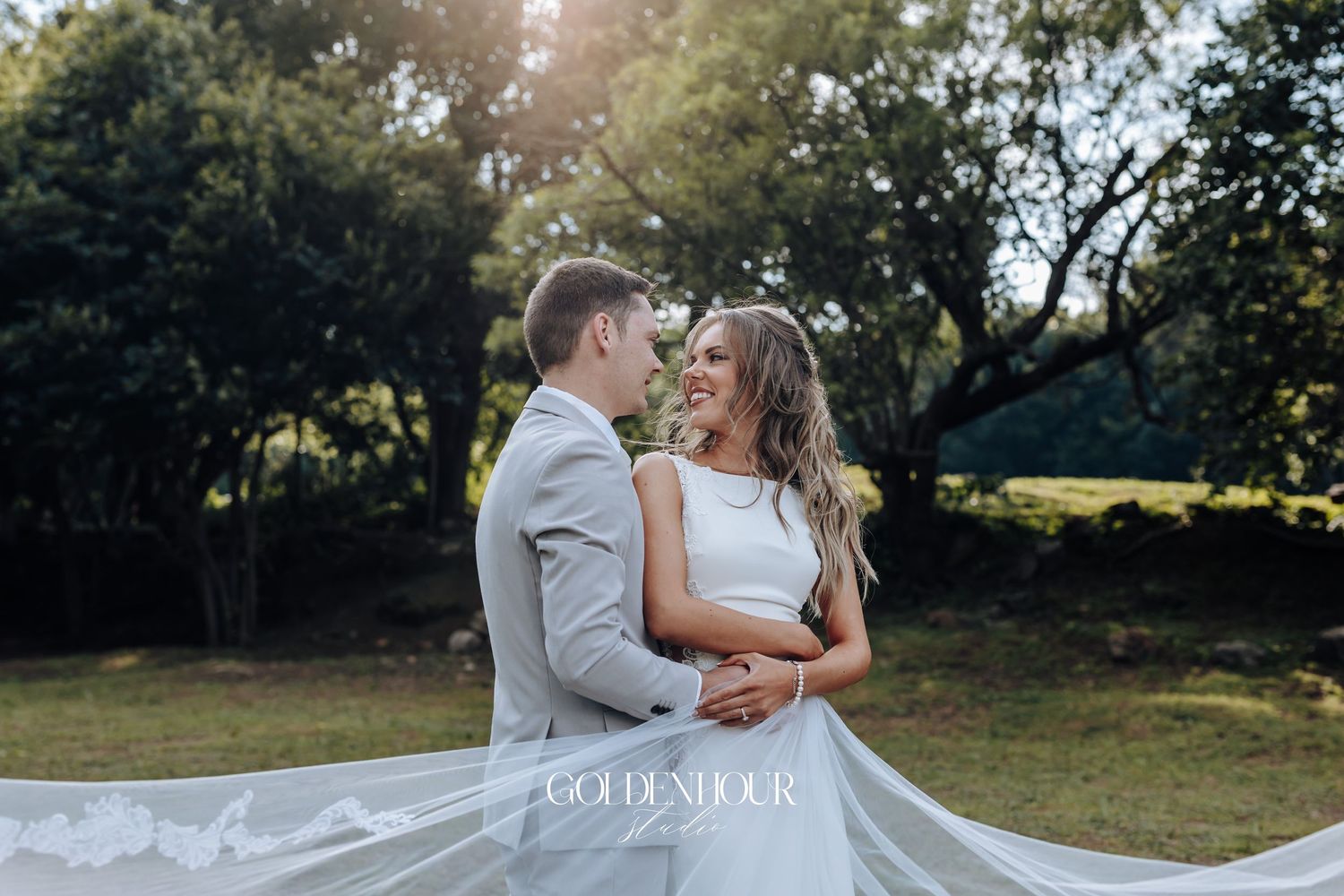 Romantic wedding couple embraces during sunset photoshoot in a scenic outdoor garden setting.