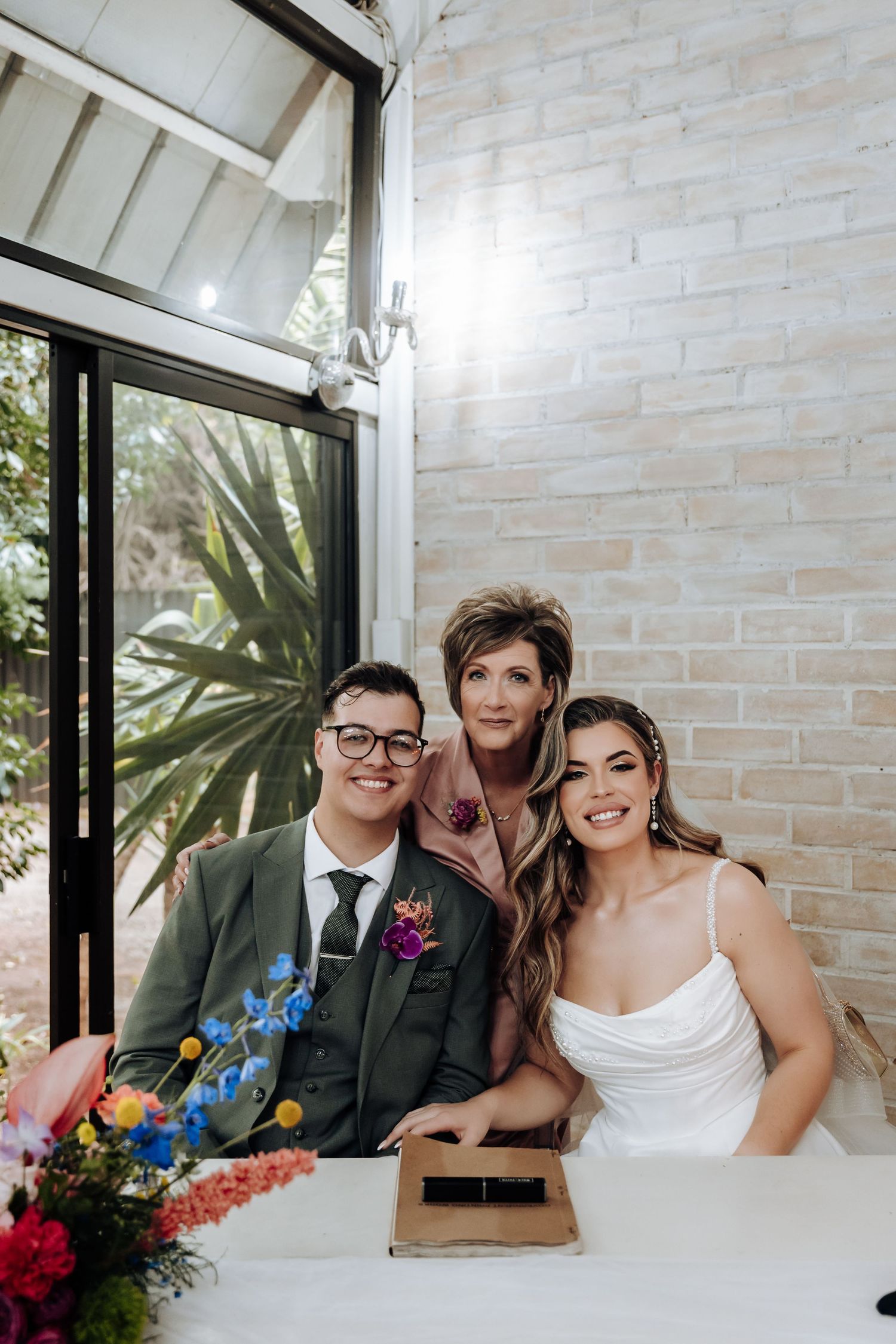 A group sits together in a bright indoor space with white brick walls and colorful flowers visible in the background.