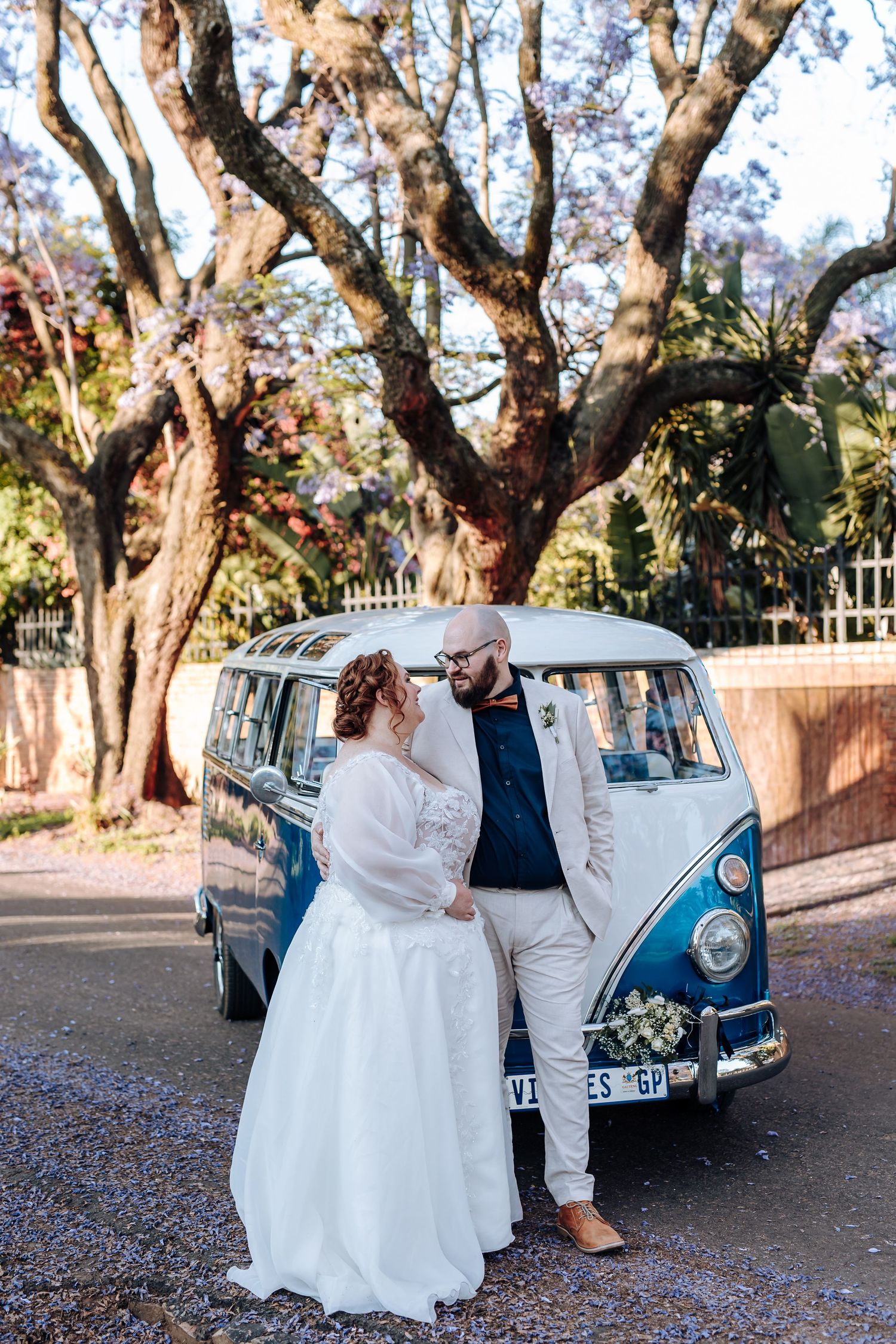 A vintage blue Volkswagen Beetle parked under trees serves as a backdrop for a romantic outdoor photoshoot.
