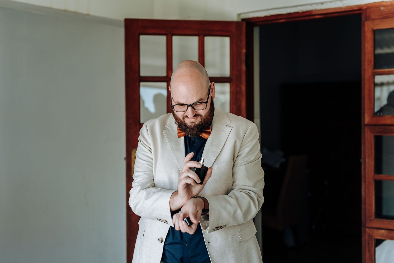 A person in a white suit jacket smiles while looking at their smartphone in a dark hallway.