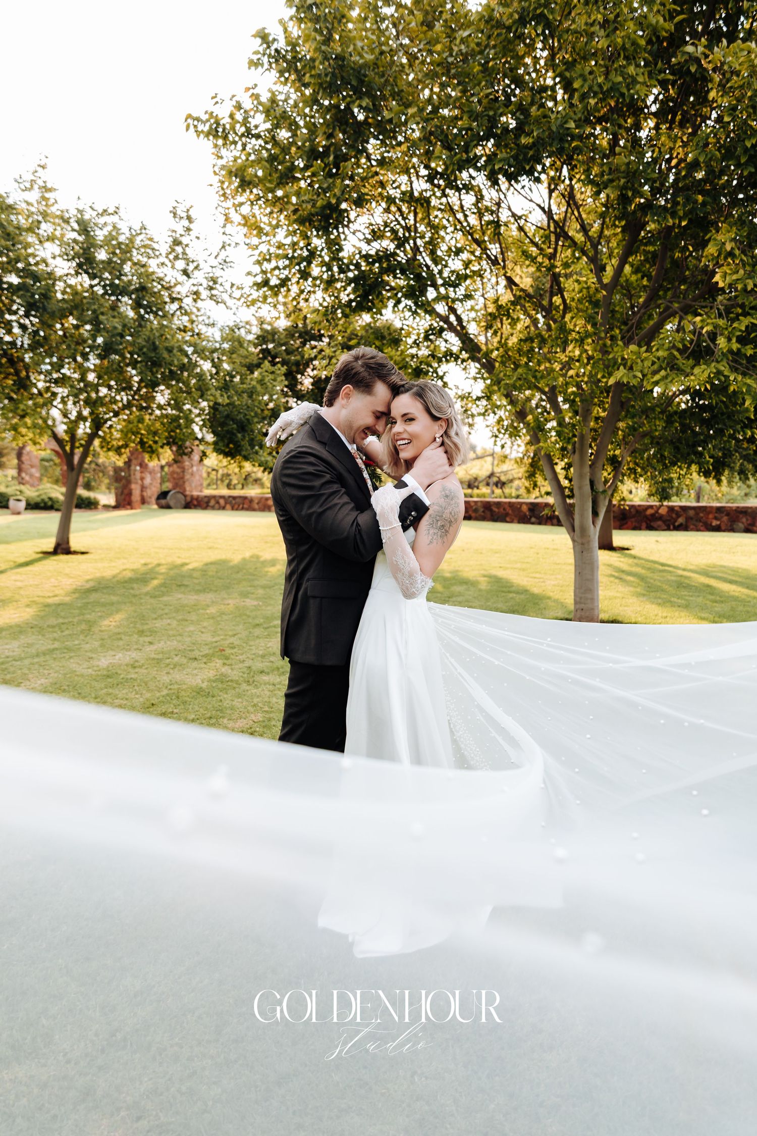 Romantic wedding portrait with flowing veil in golden sunset light.