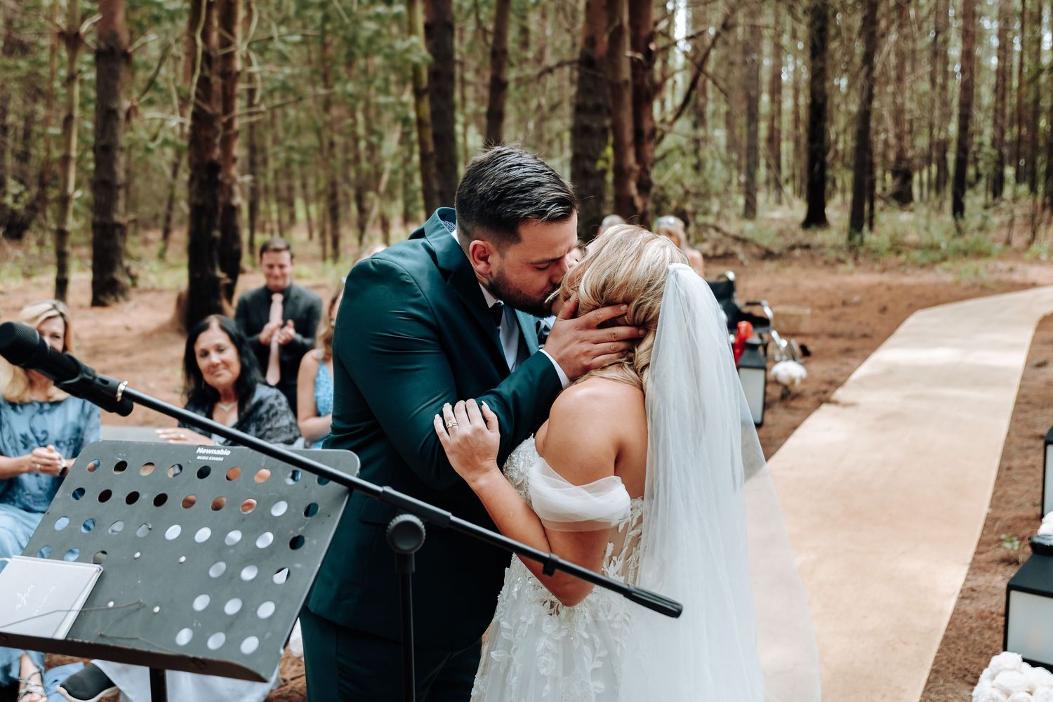 A couple shares their first kiss as newlyweds during an outdoor forest wedding ceremony.