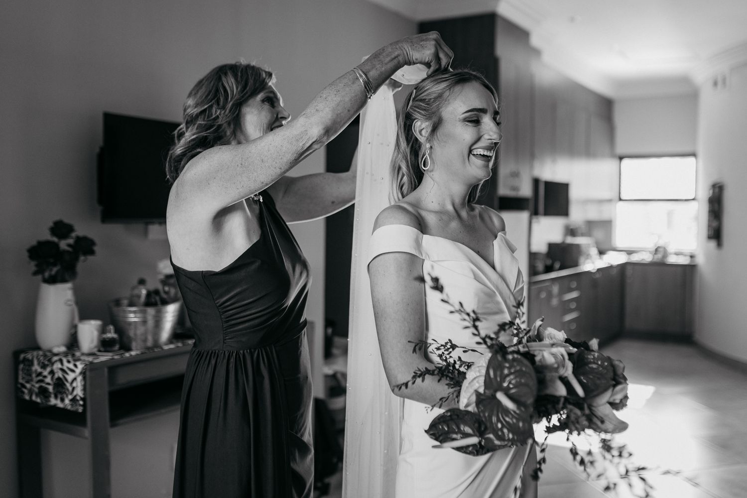 Black and white candid moment of wedding preparations with flowing white dress.