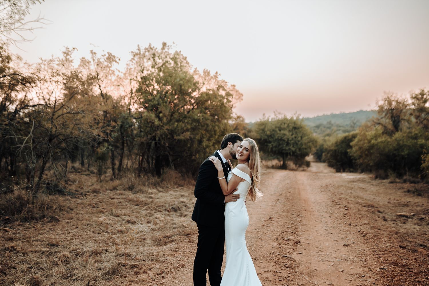 An intimate wedding portrait captured on a scenic dirt path during golden hour.
