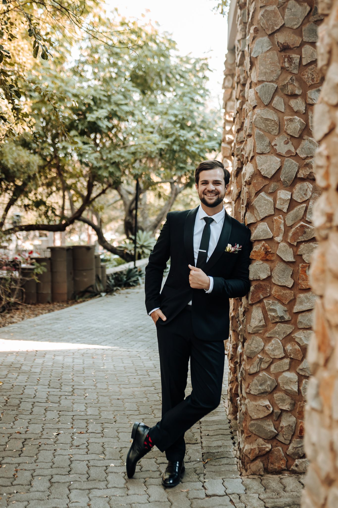 Well-dressed person poses confidently against stone column on brick pathway.