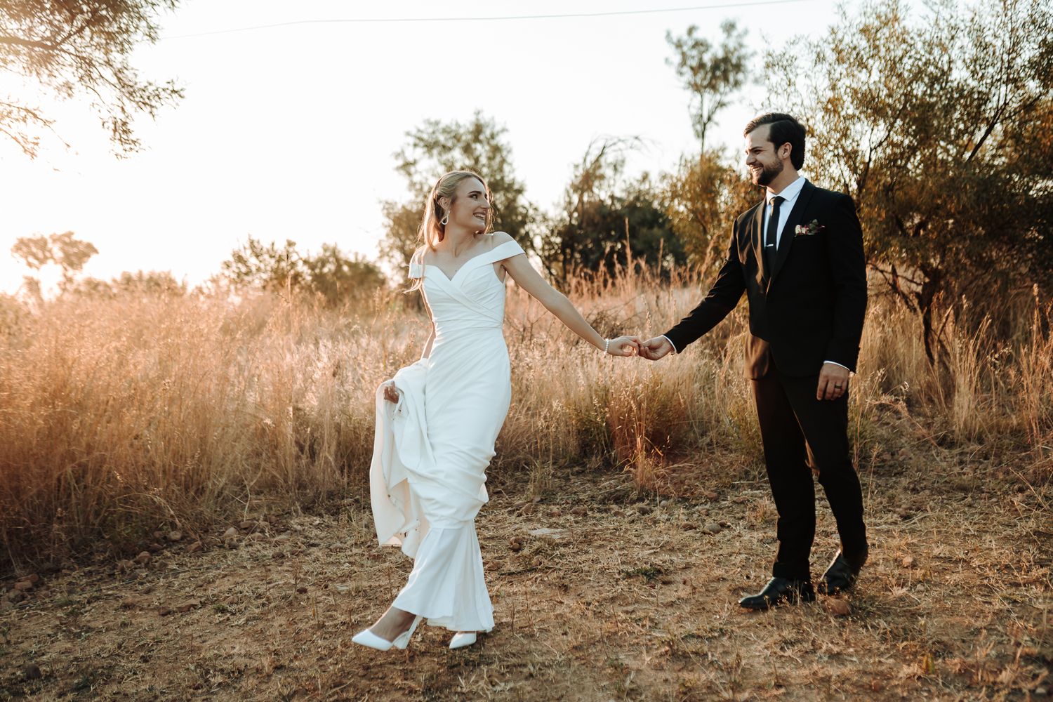 Playful wedding moment as bride in elegant white gown dances with groom in outdoor setting.