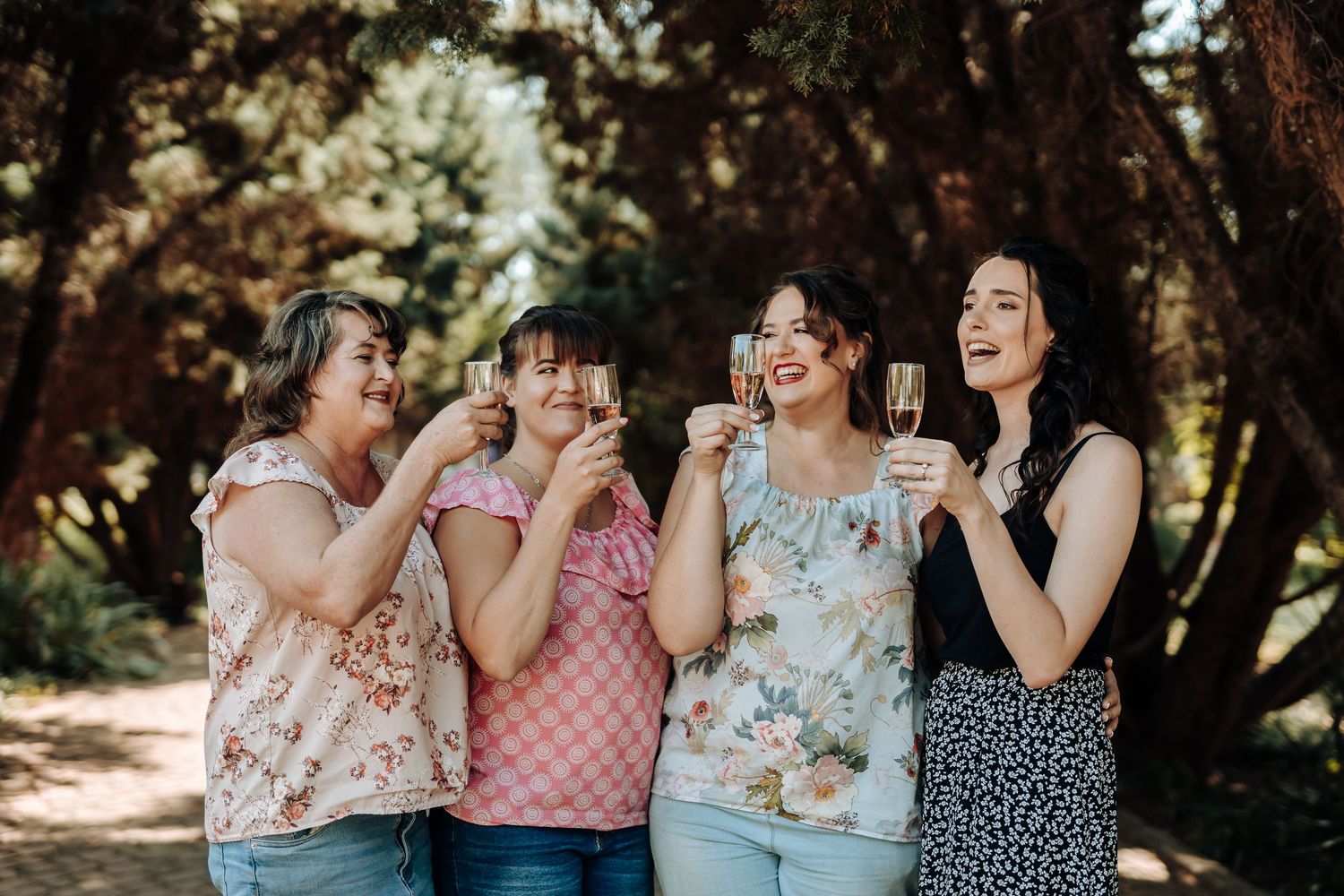 Four friends sharing joyful moments with drinks in a sunlit forest setting.